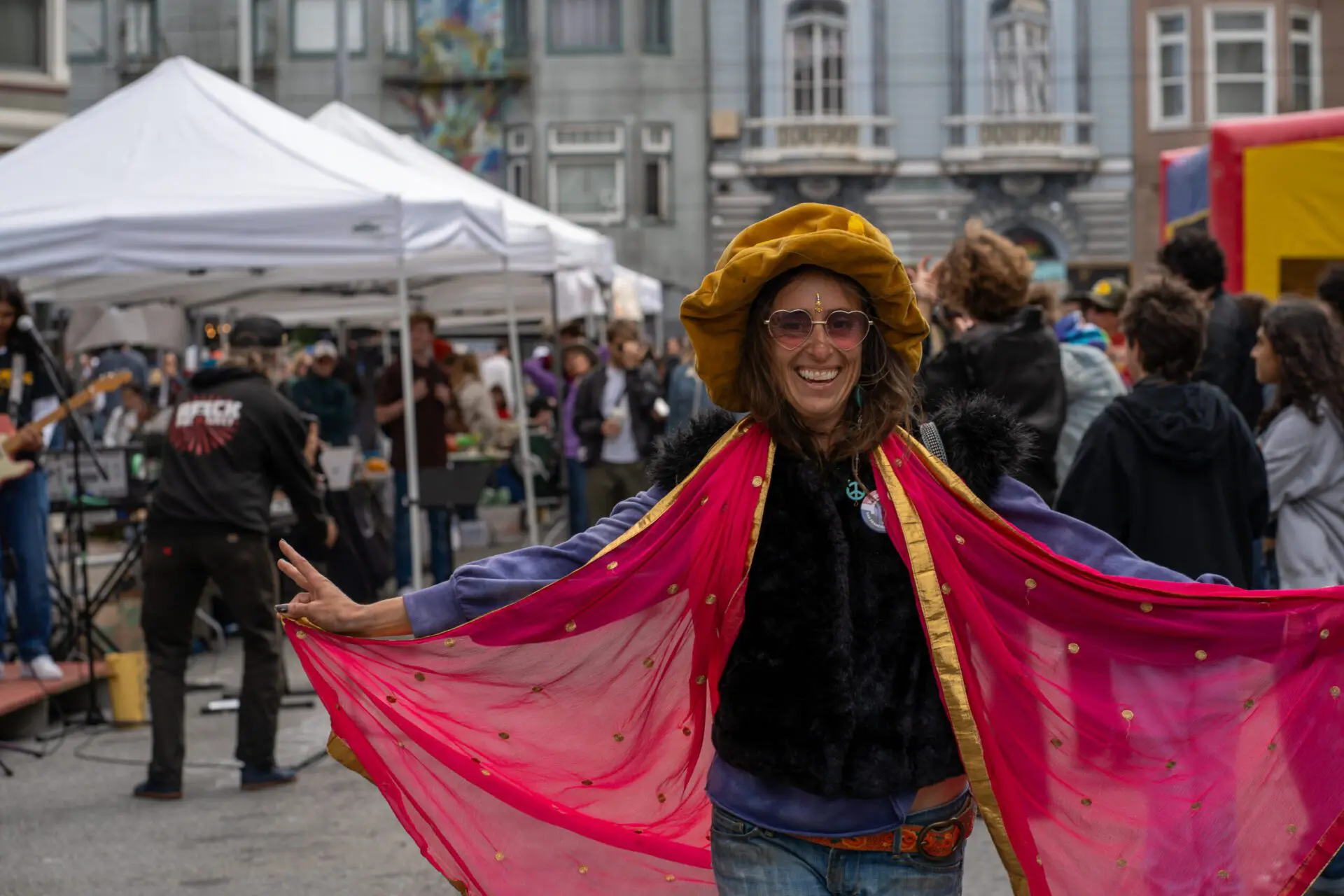 Woman in a gold hat and colorful cape smiling at the crowd