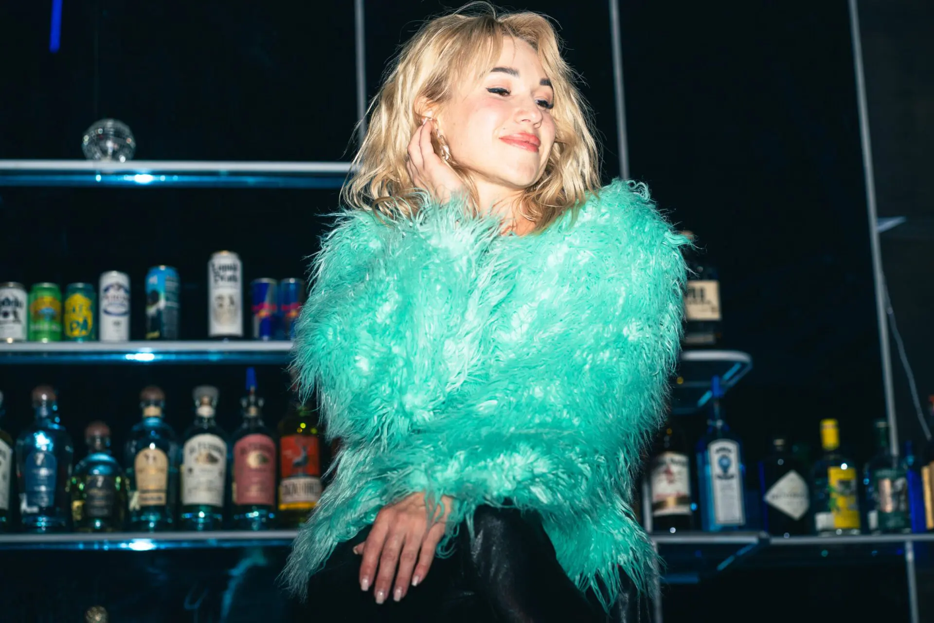 Woman in a fluffy teal jacket posing near the bar area.
