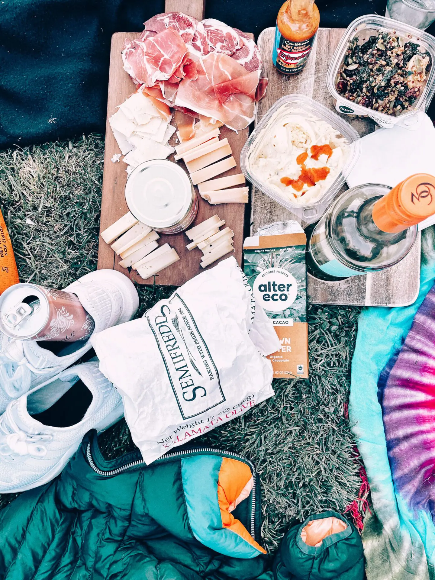 Flat lay of picnic snacks, drinks, and blankets on the grass.