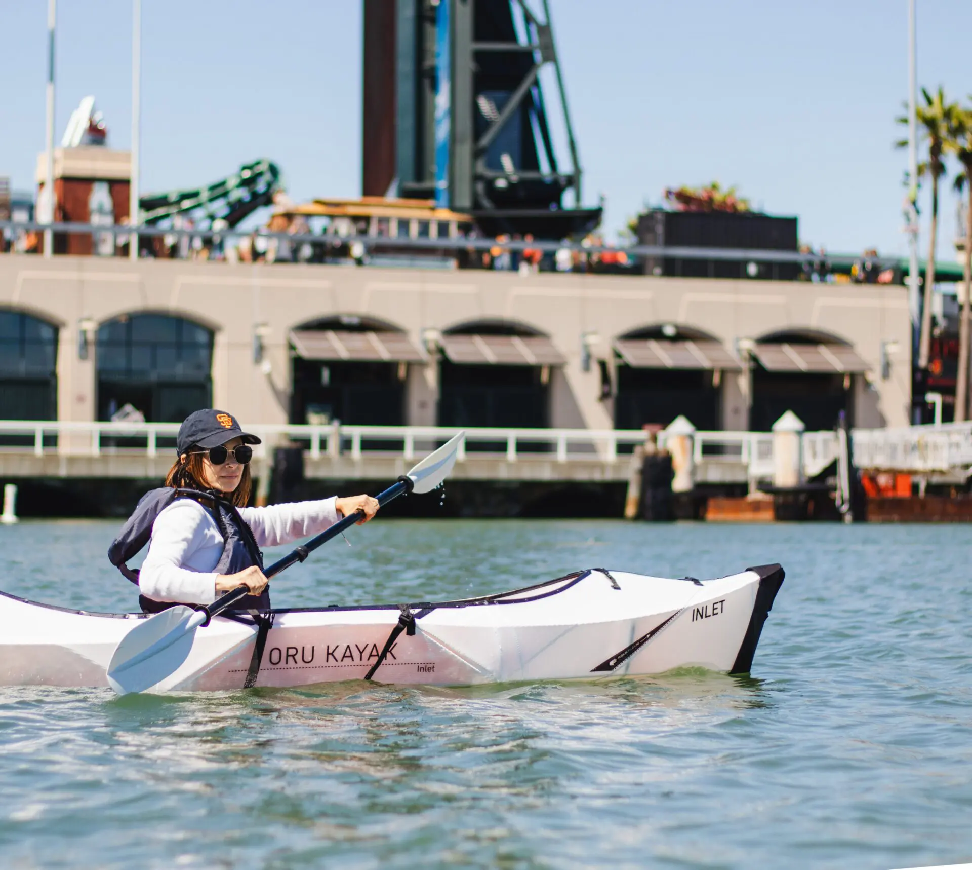 Woman in an Oru kayak paddling along the water facing the stadium.
