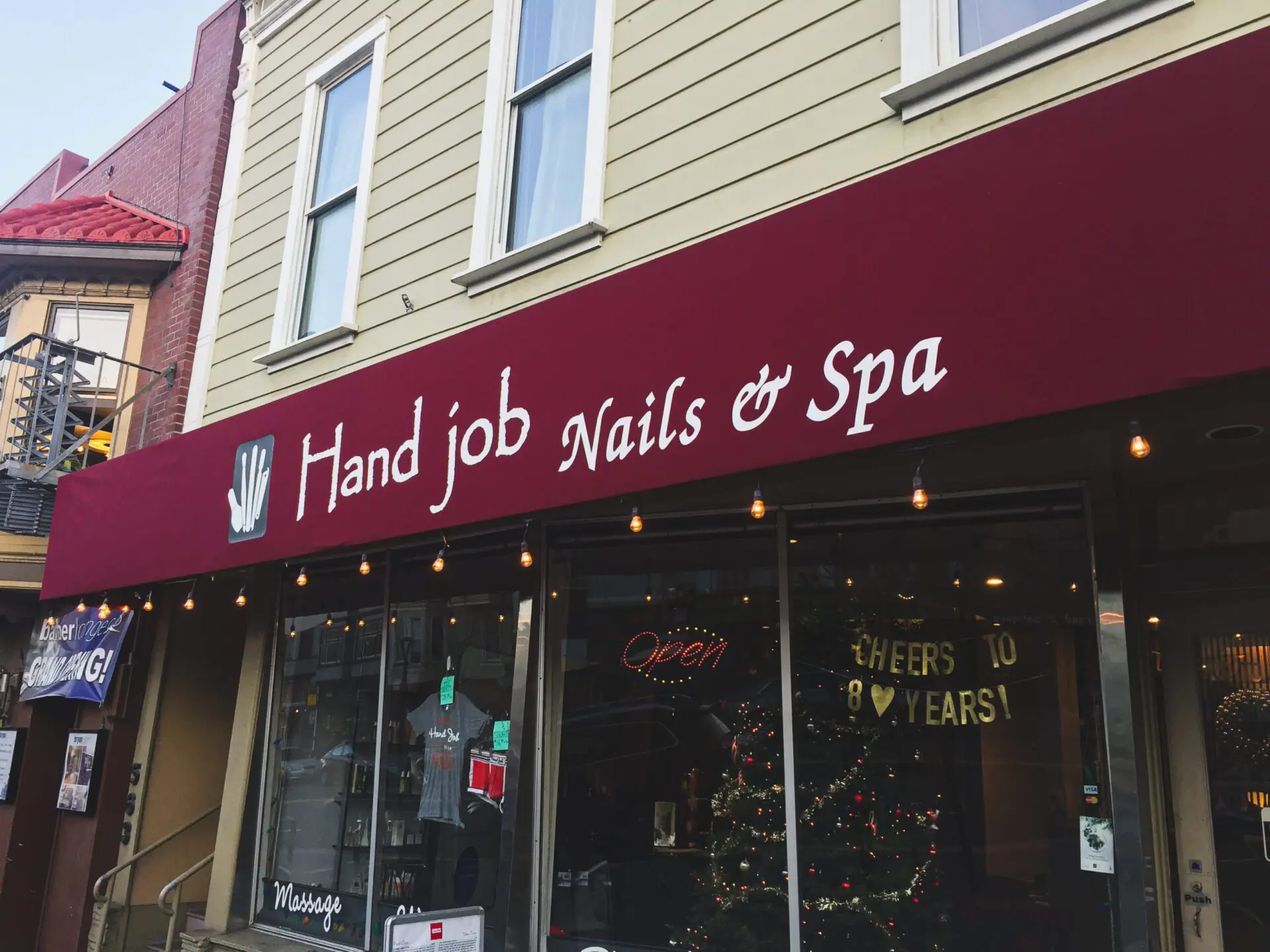 Storefront of Hand Job Nails & Spa with its maroon sign above the entrance