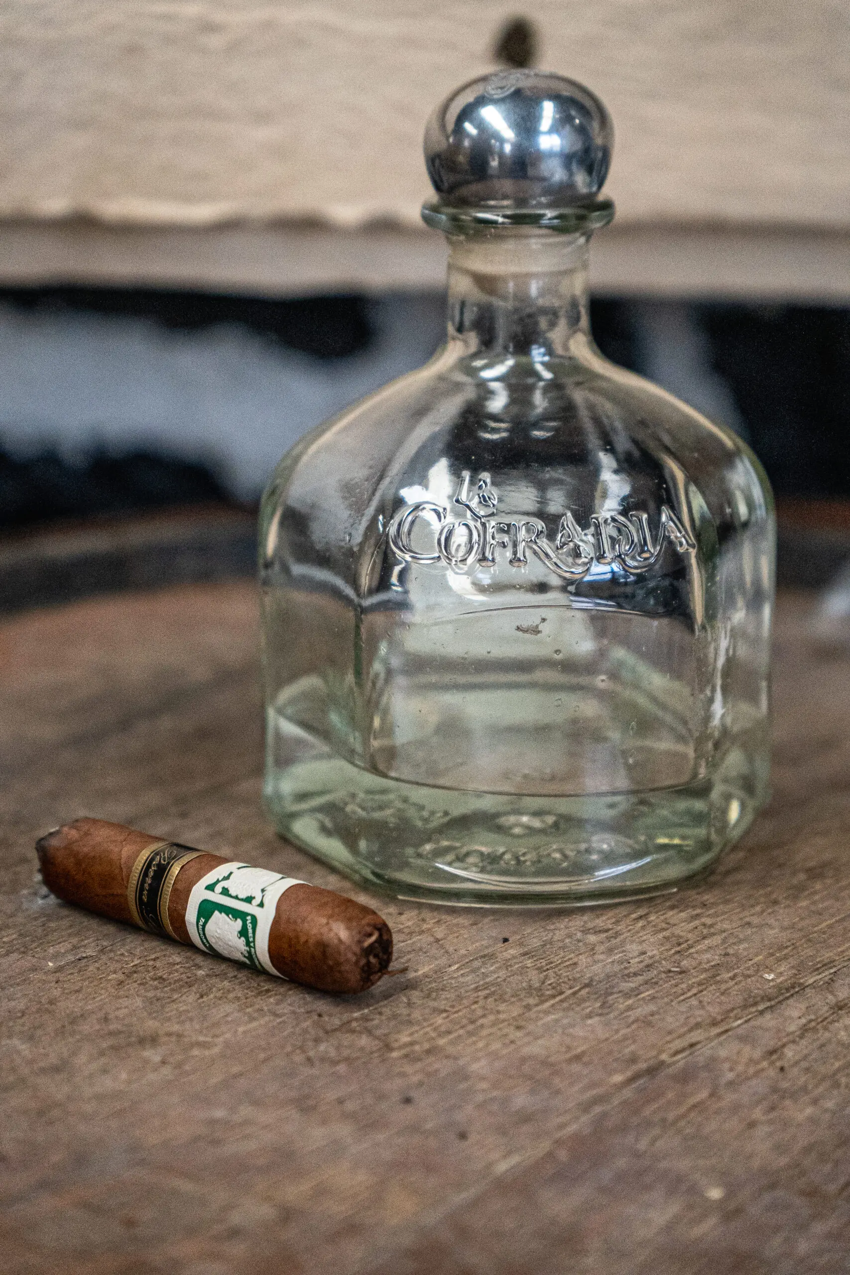 A cigar resting on a wooden surface beside an empty glass bottle.