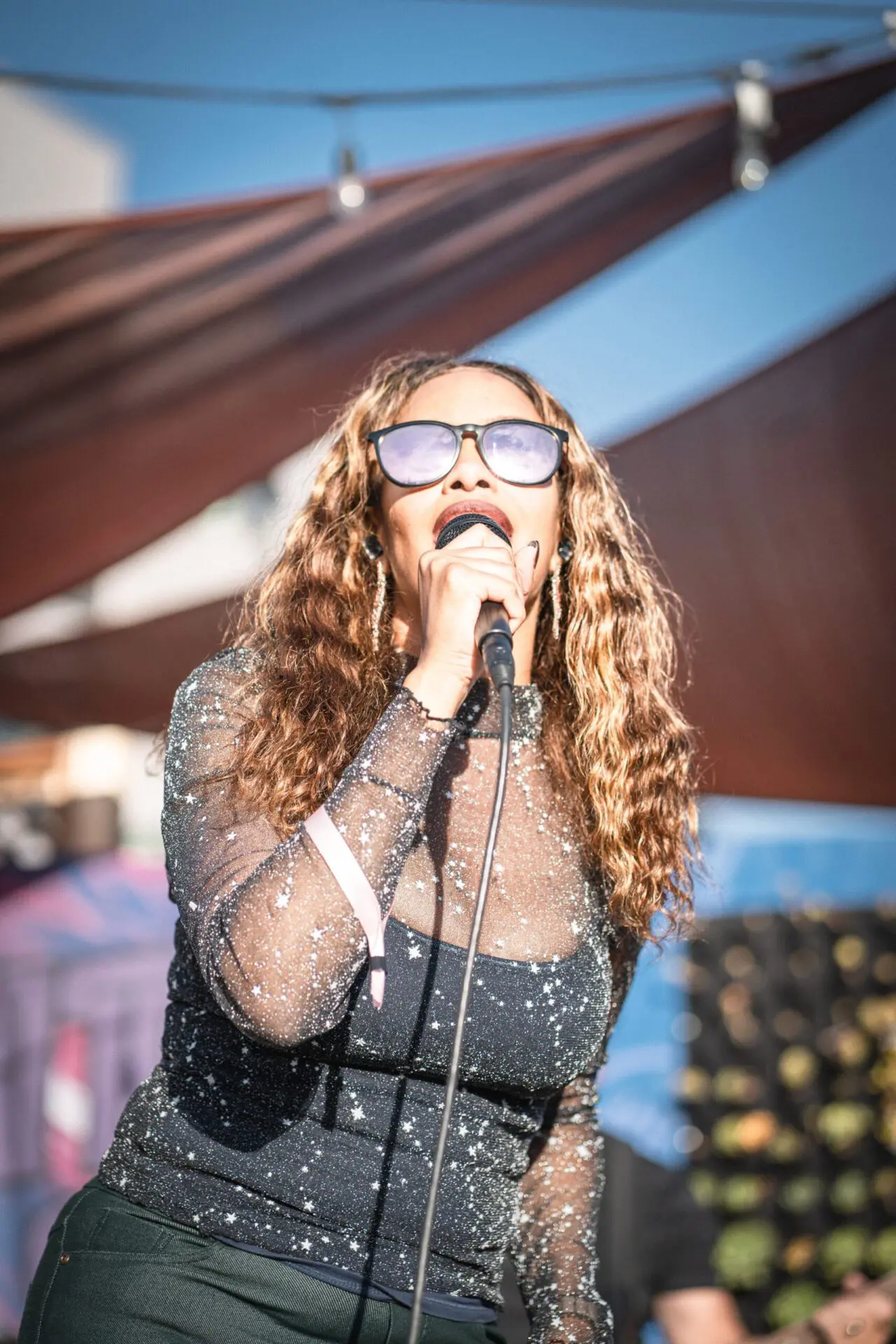 Singer performing onstage at Spark Social under the shade sails