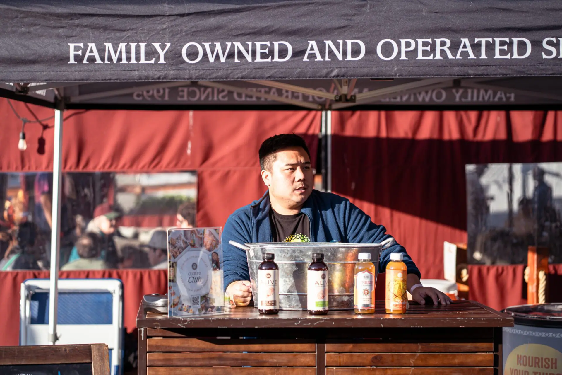 Family-owned vendor serving cider samples at Spark Social during the Cider Festival, standing behind a display of bottled drinks