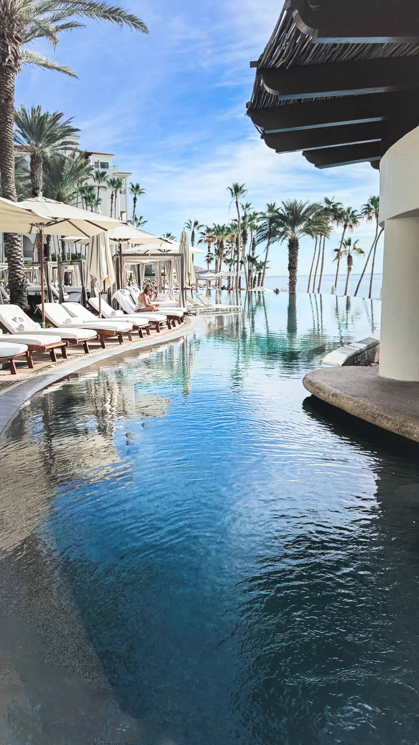 Luxurious poolside with lounge chairs and palm trees under a clear sky.