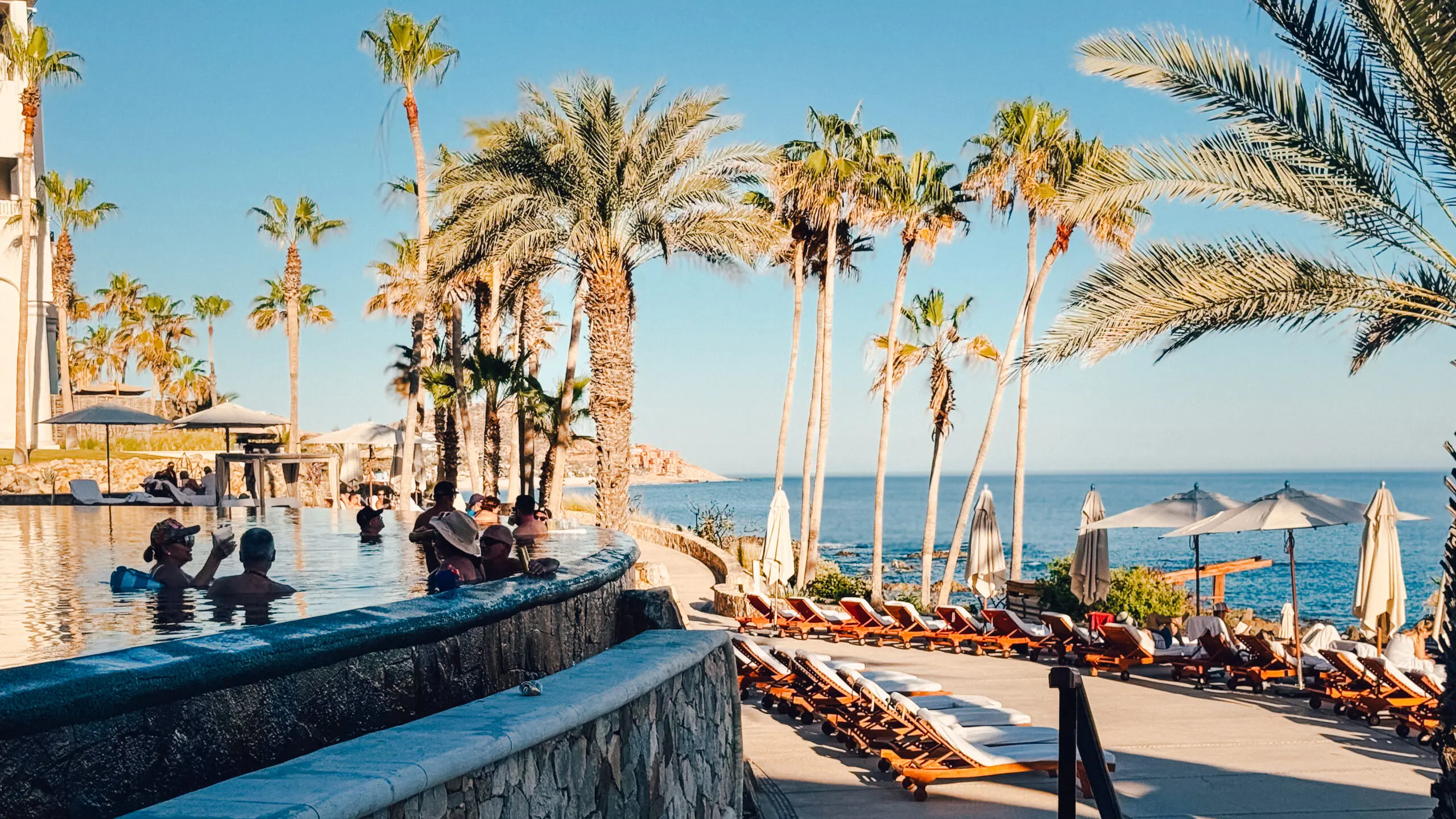 Luxurious poolside with palm trees by the ocean at sunset.