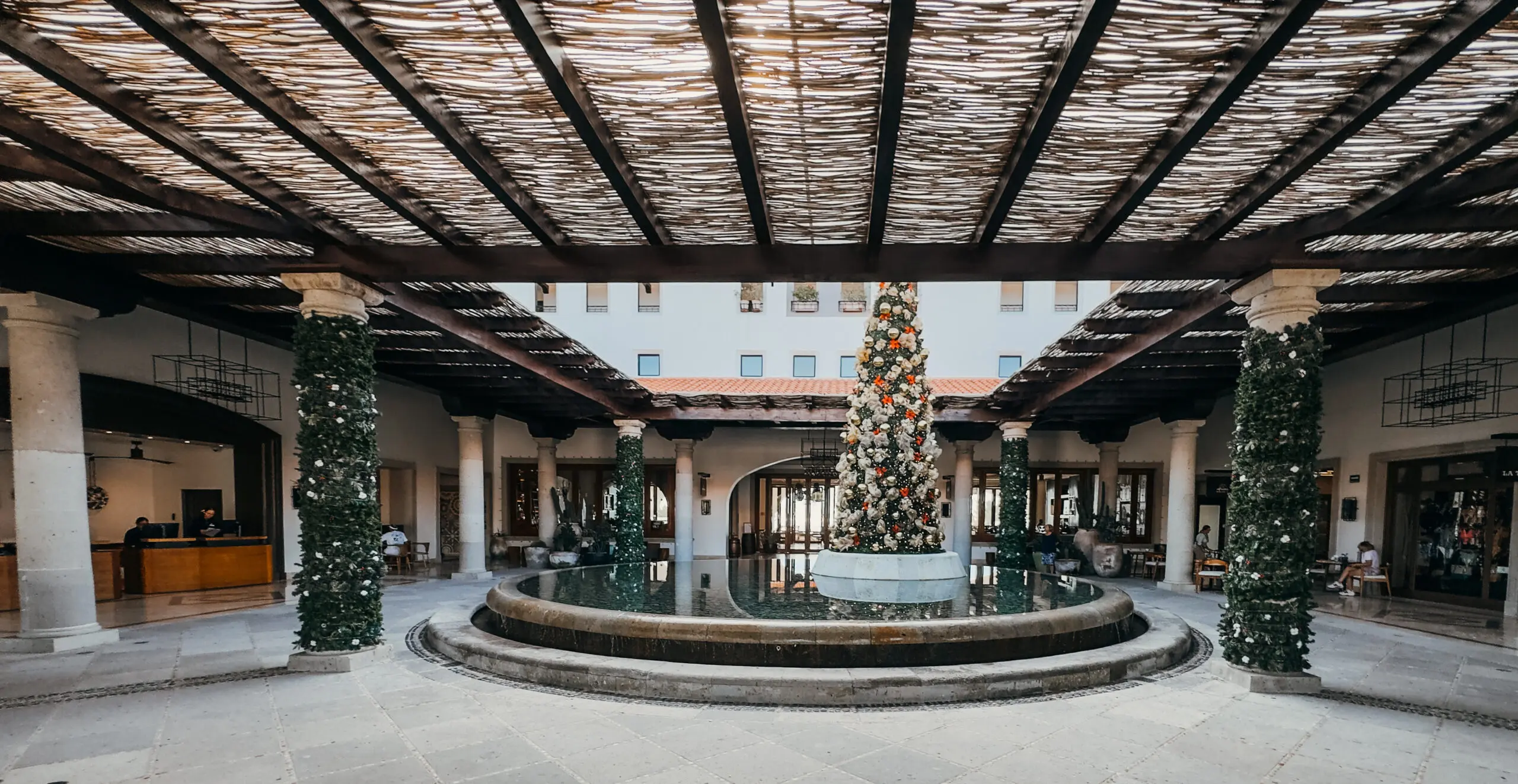 A decorated Christmas tree in the center of an open courtyard with a rustic ceiling overhead.
