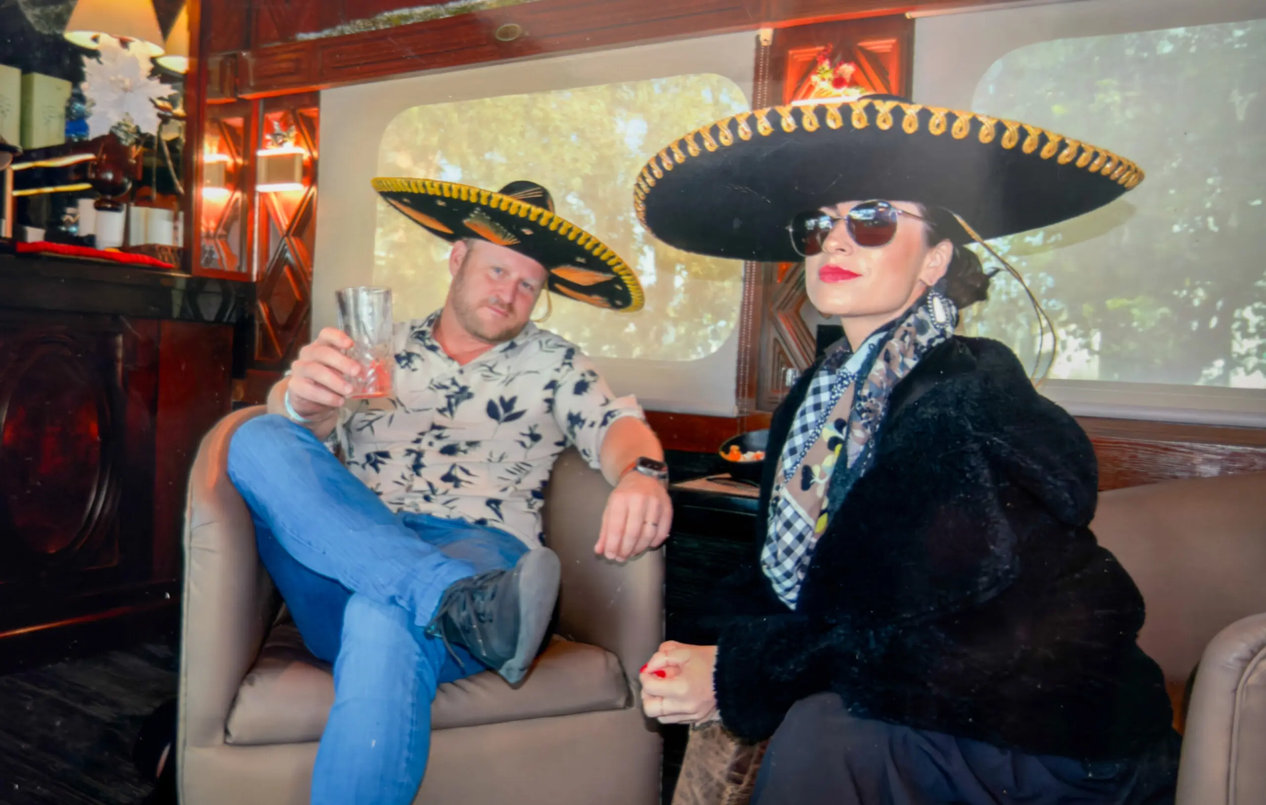 Two people wearing large sombreros and posing indoors with drinks.