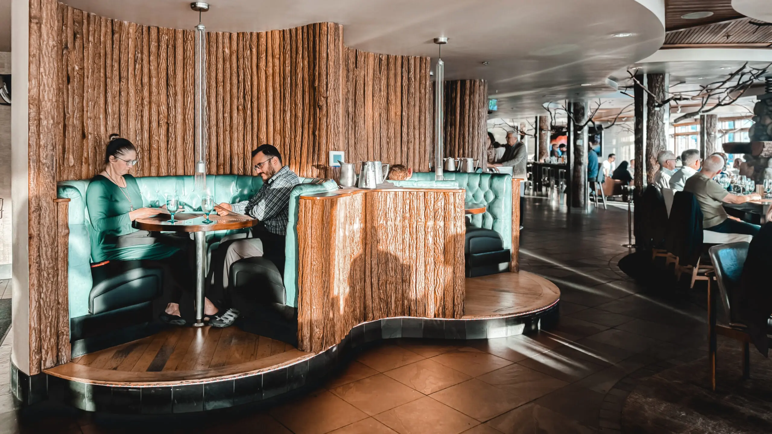 Man sitting alone in a stylish, modern cafe with wooden decor and teal accents.