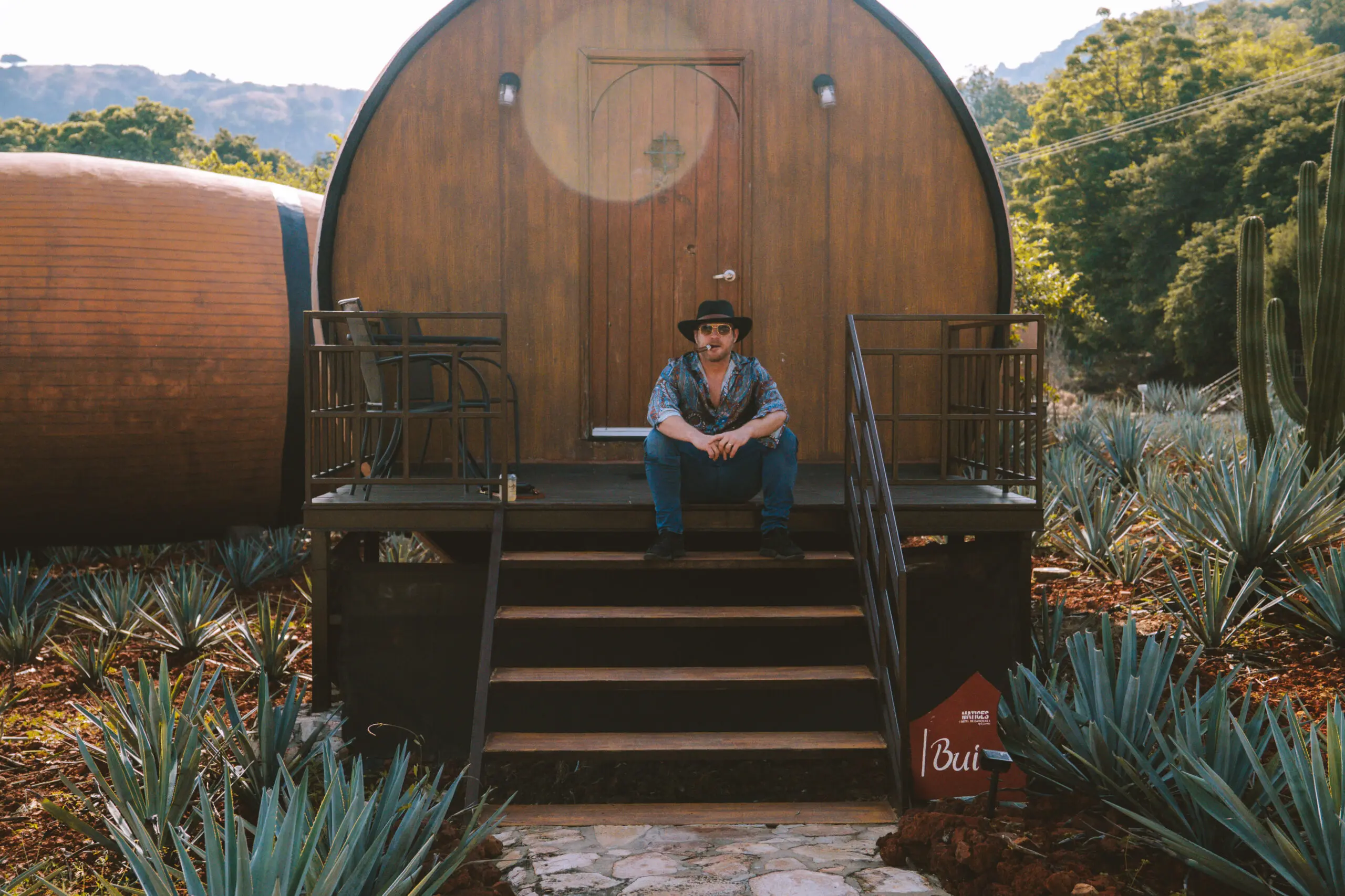 Person sitting on wooden steps outside a barrel-shaped cabin.