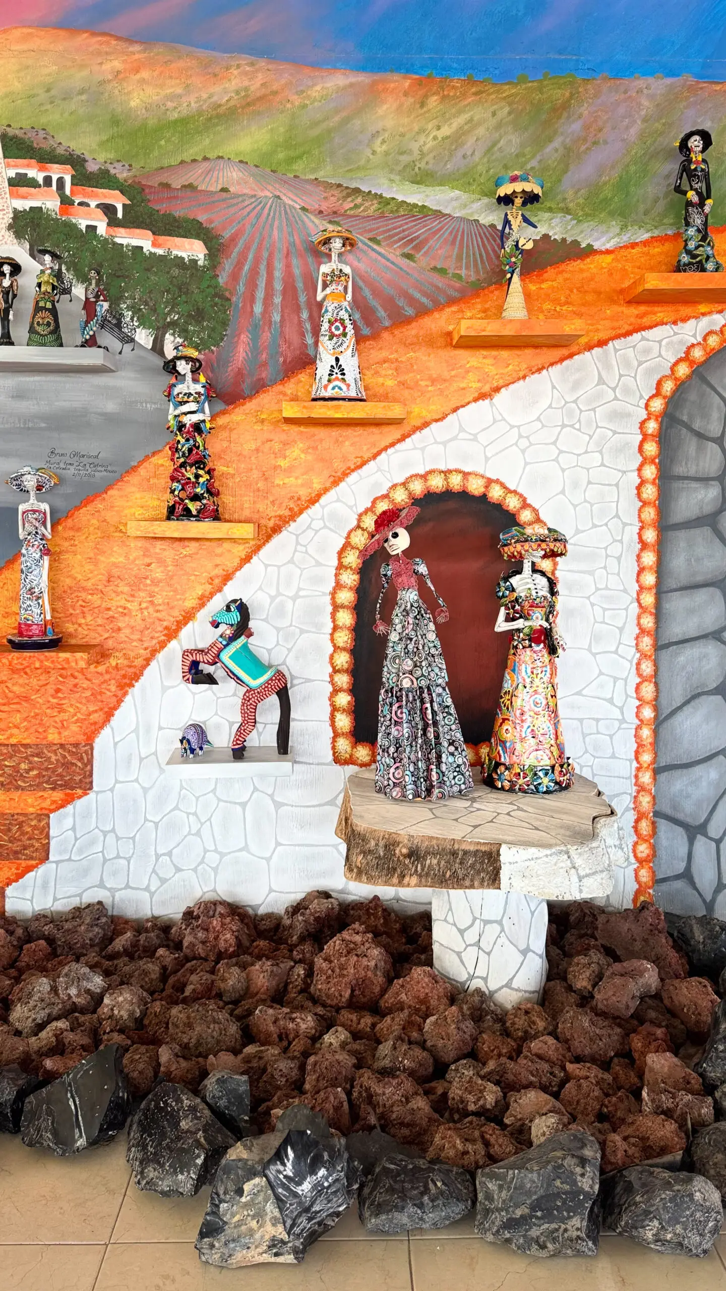 Colorful traditional Mexican sculptures on a vibrant orange and white backdrop.