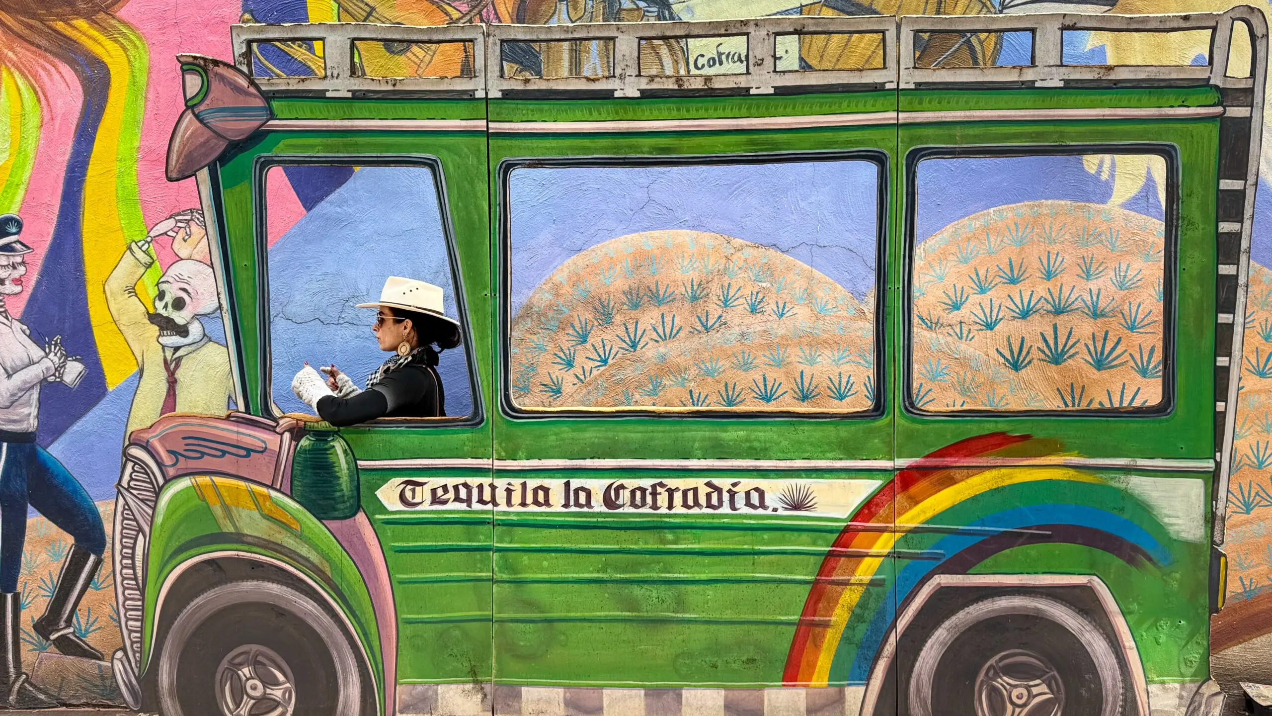 Colorful bus with a driver and scenic hills in the background.