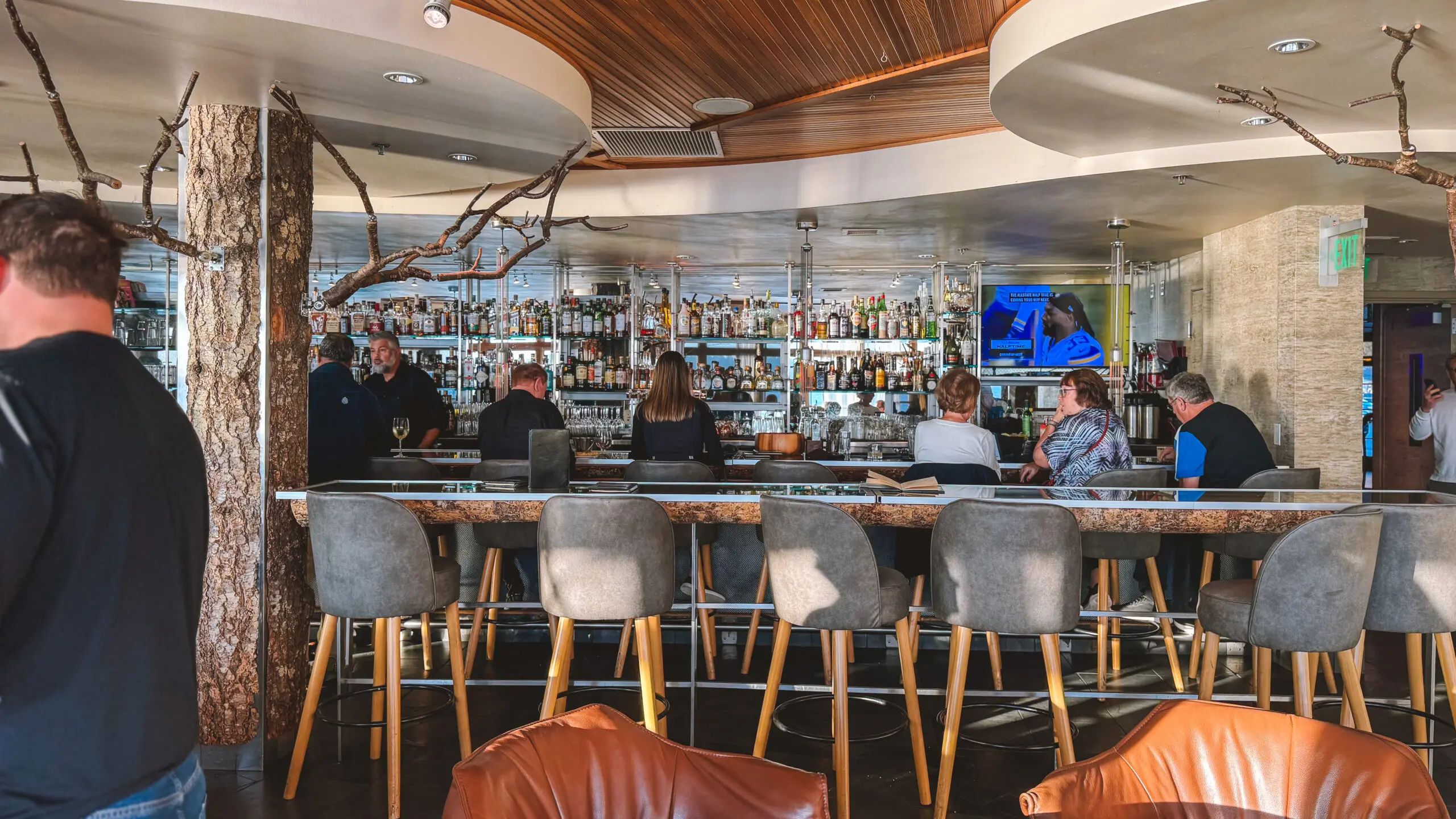 People seated at a modern bar with a wooden ceiling and a TV screen.