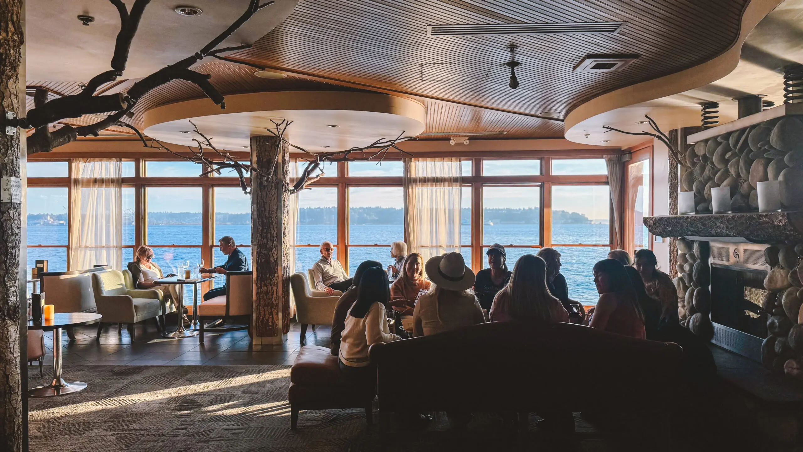 People enjoying a scenic view from a cozy indoor lounge with large windows.