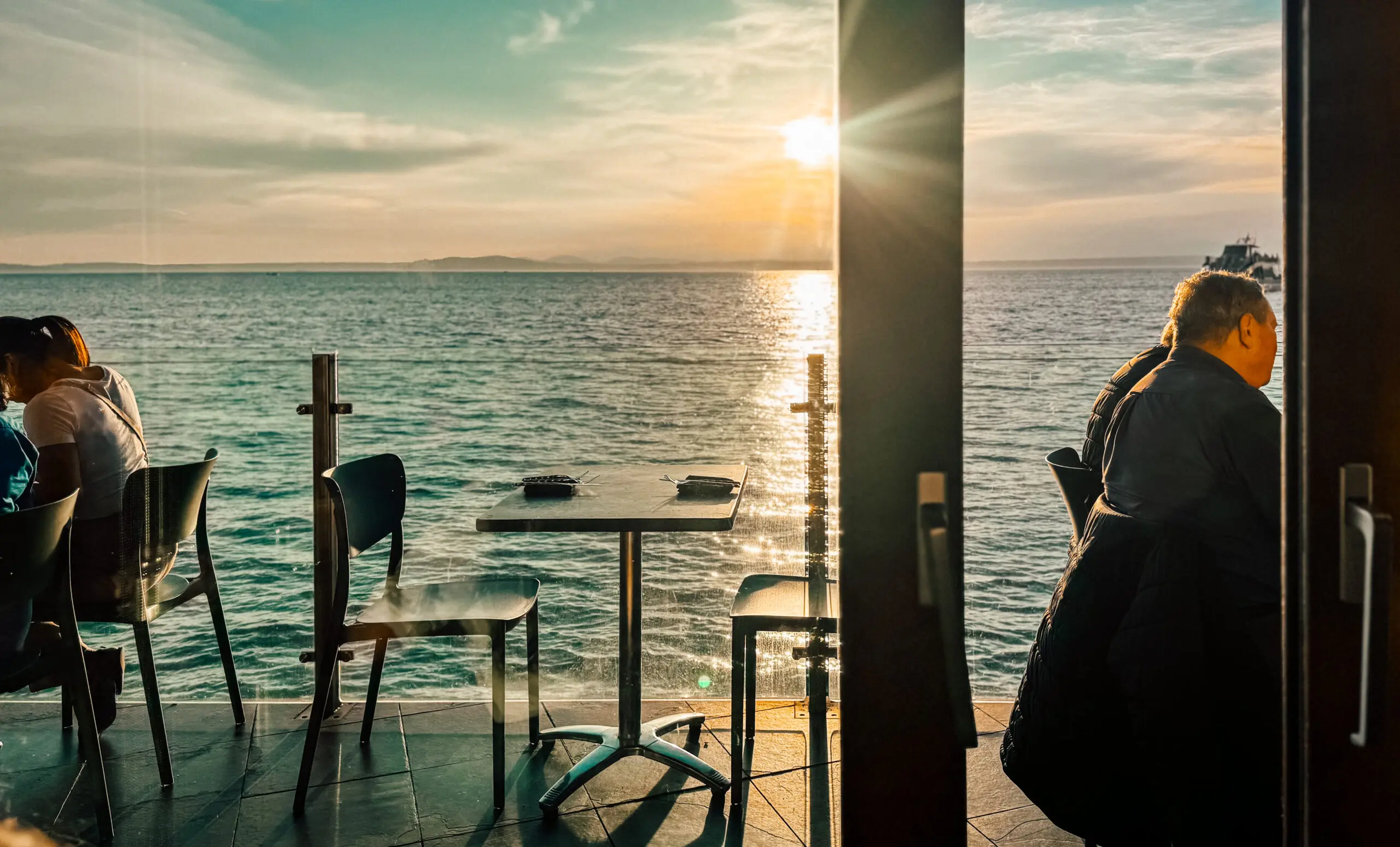 Sunset view from a cozy seaside café with empty tables and chairs.