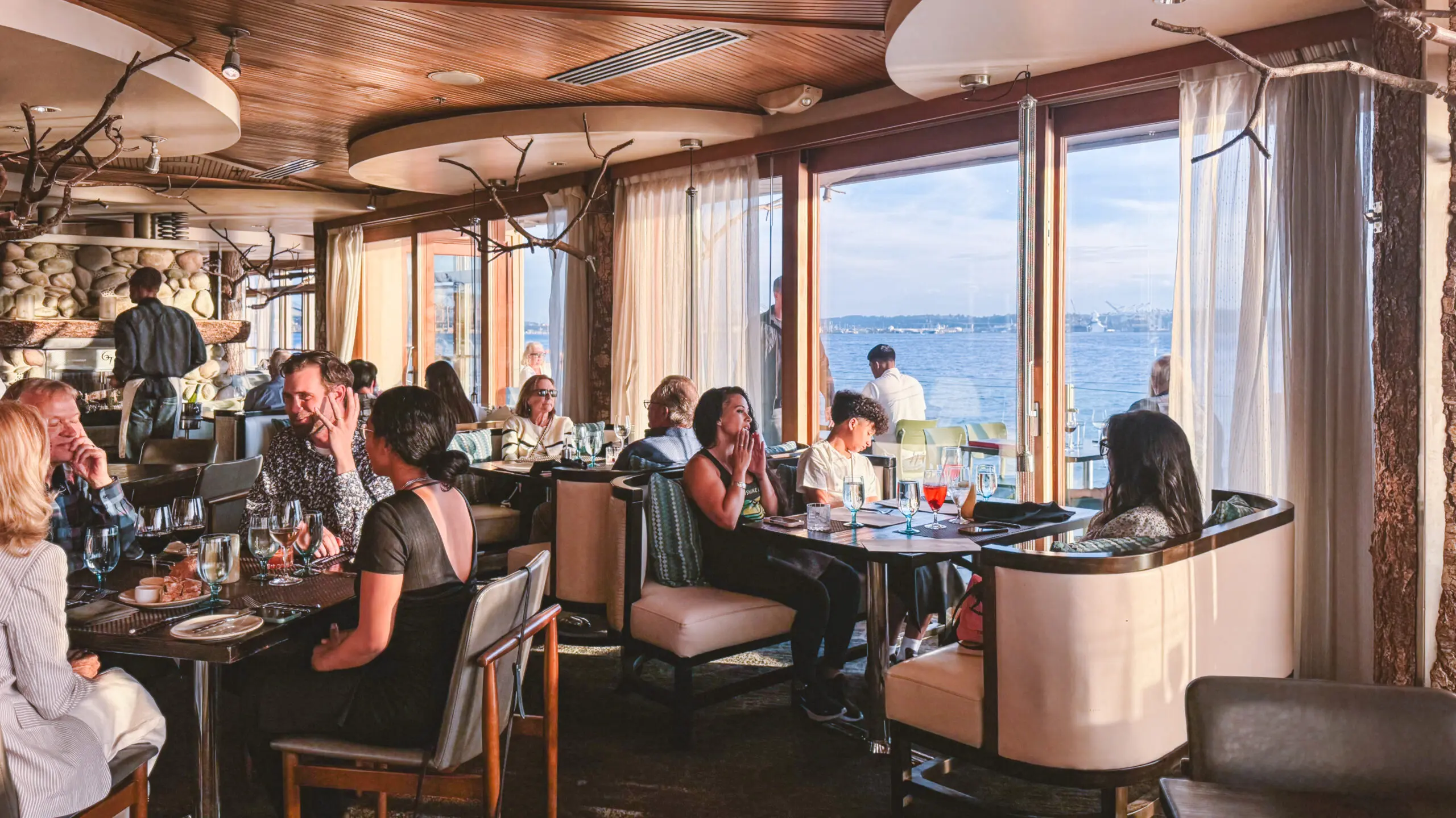 People dining in a cozy restaurant with a sea view through large windows.