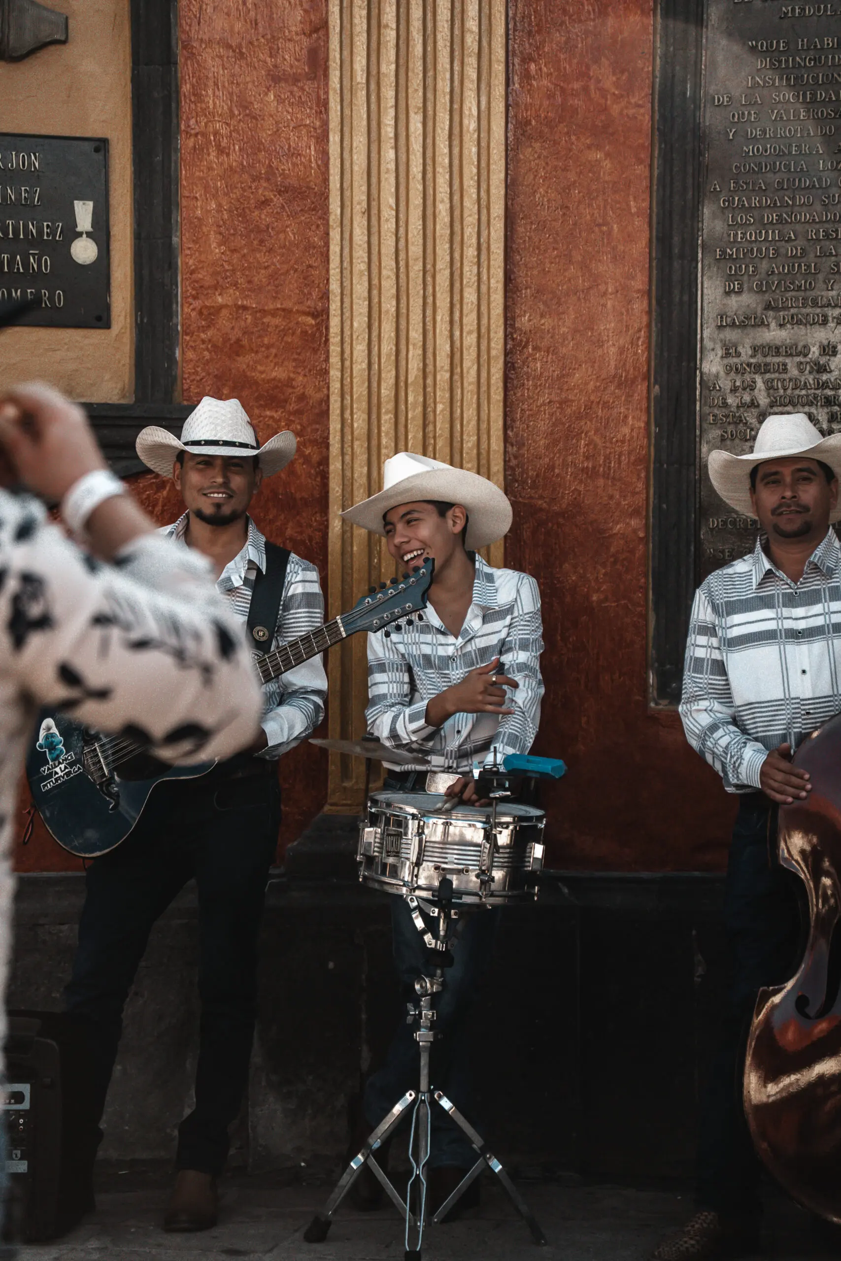 A mariachi band performs with guitars and a drum in traditional attire.