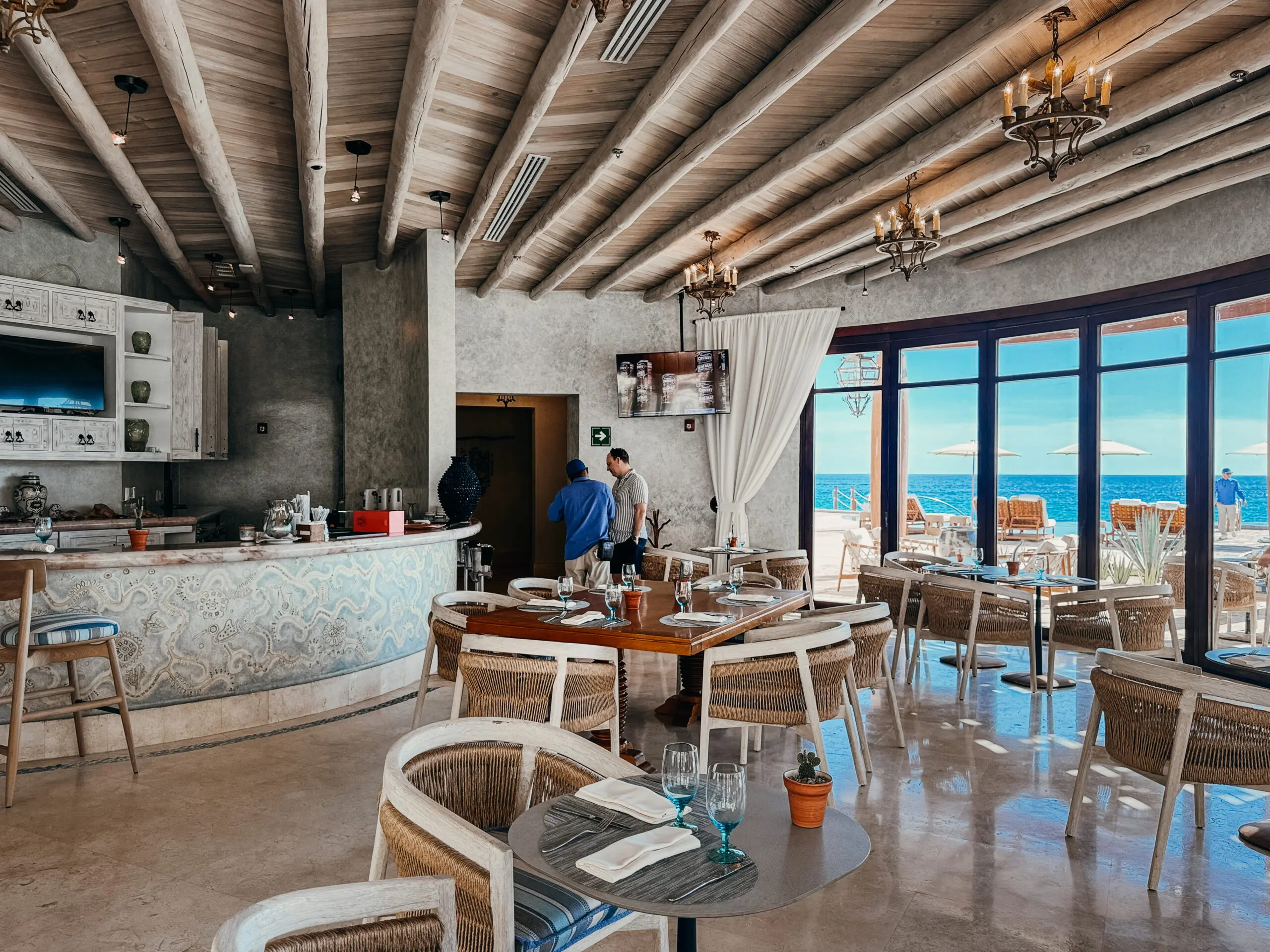 Cozy modern cafe with wooden ceiling and ocean view through large windows.