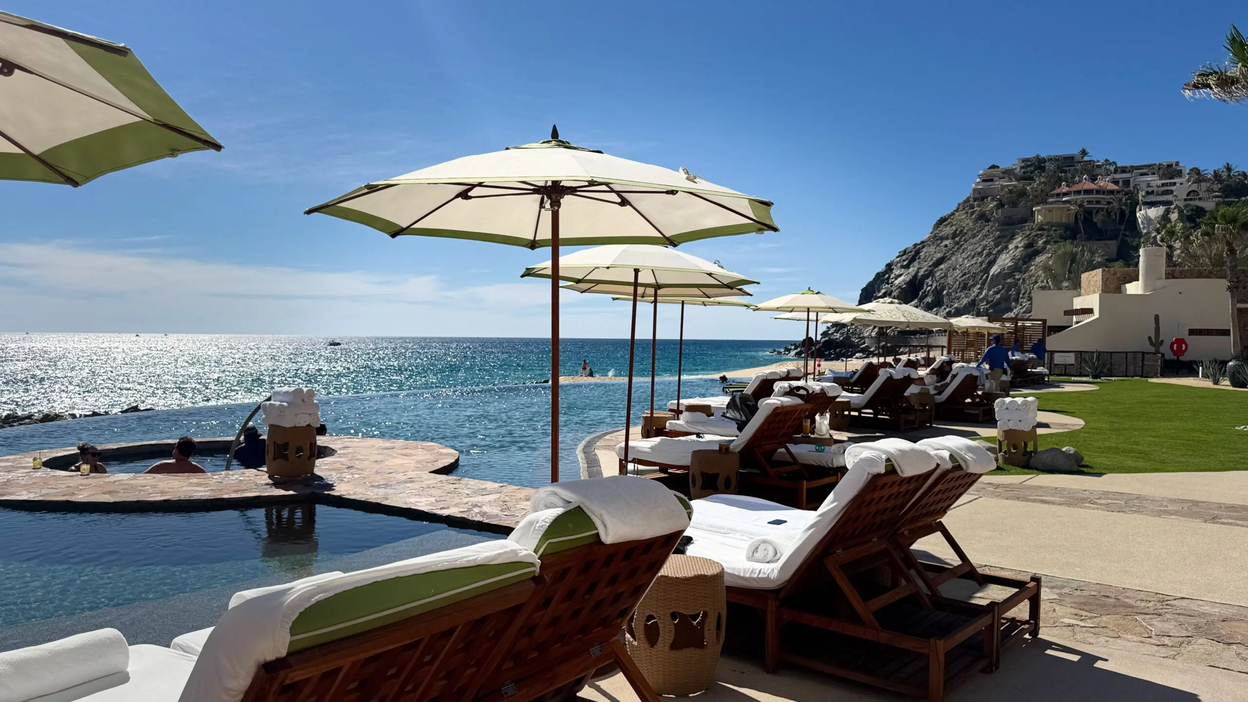 Luxurious sun loungers with umbrellas by a serene ocean view and rocky cliffs.