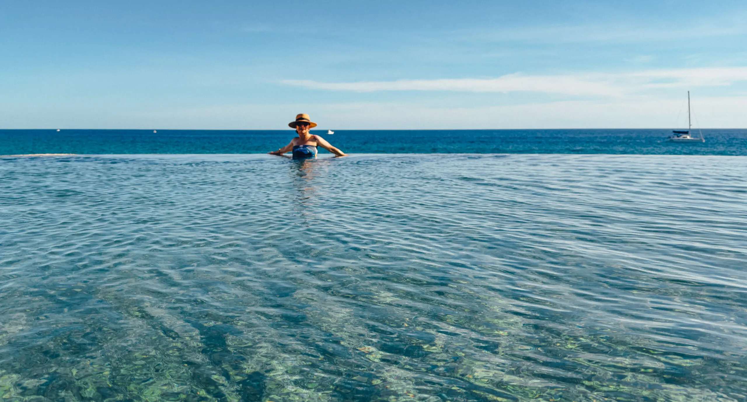 Person sitting peacefully in shallow, clear ocean water under a blue sky.