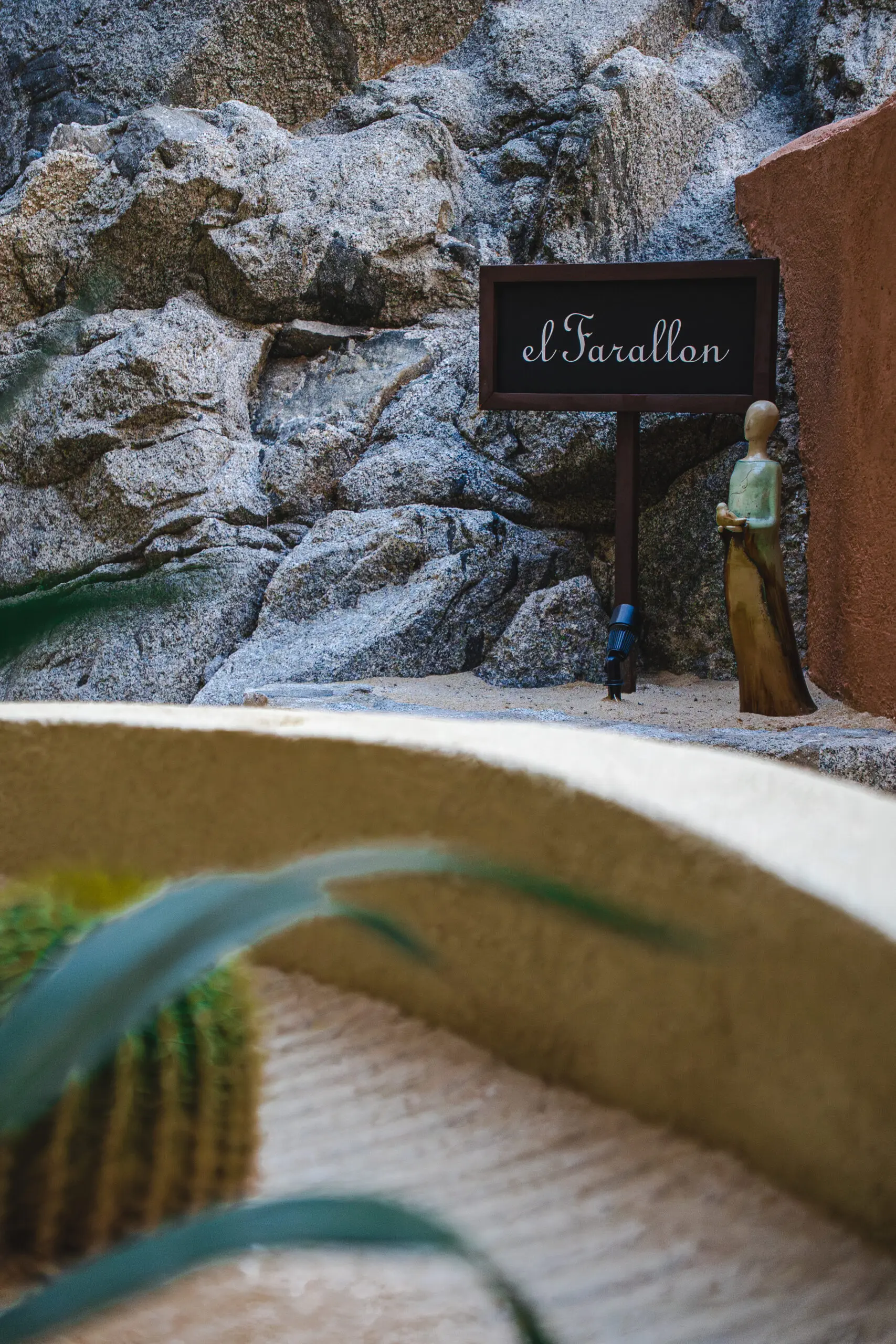 A miniature figure stands by a sign on a rocky sandy terrain.