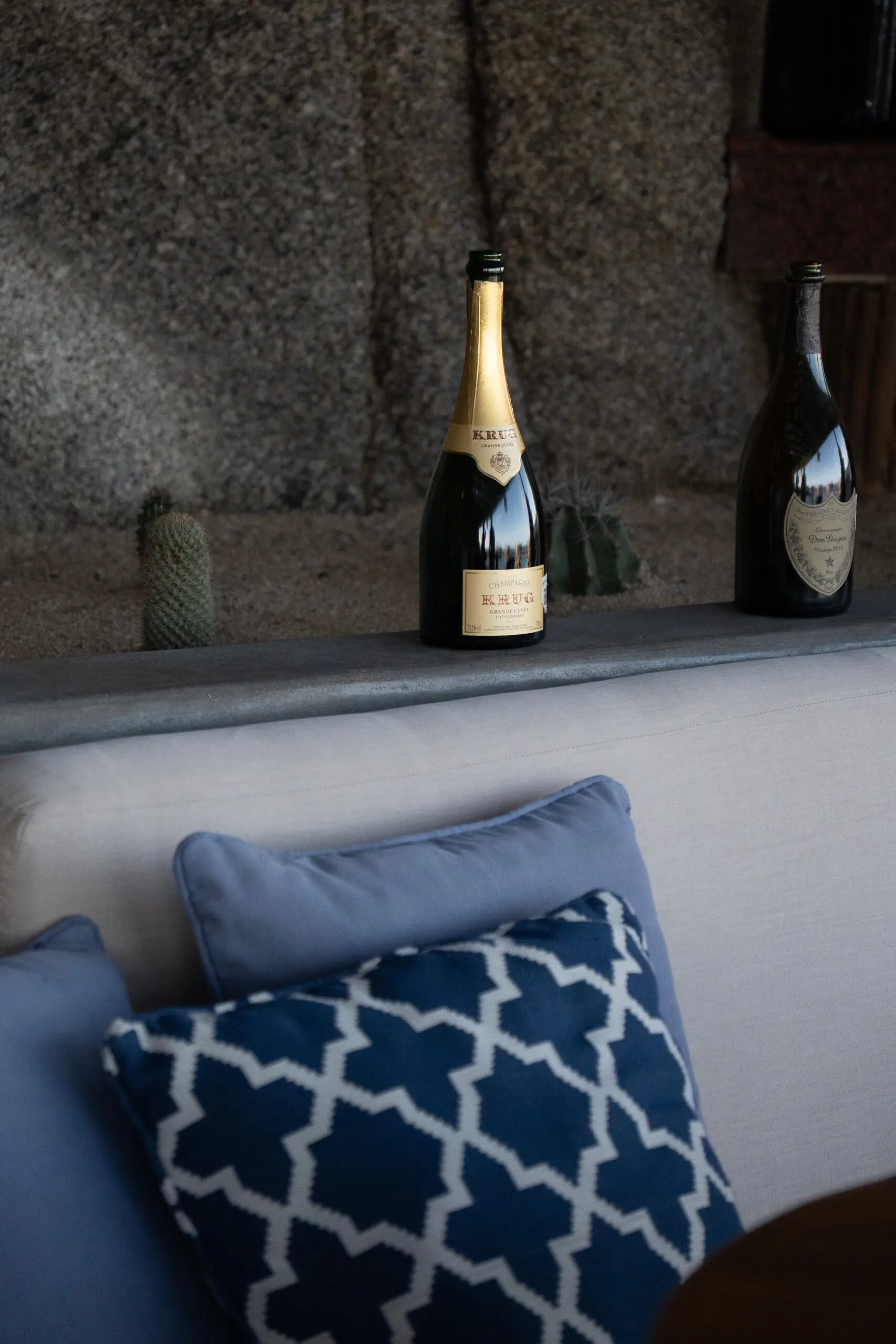 Champagne bottles on a stone ledge with cozy pillows nearby.