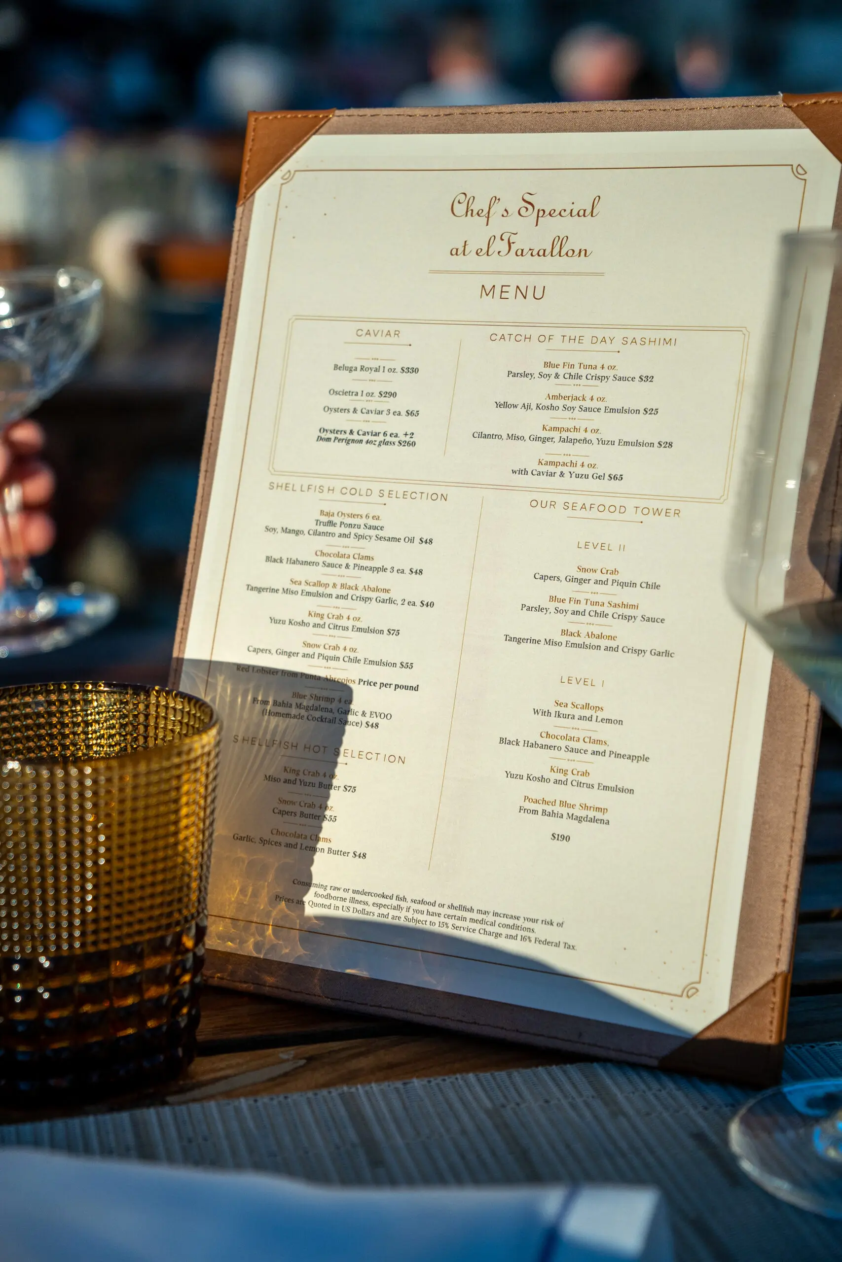Close-up of a restaurant menu on a wooden stand with textured glassware nearby.