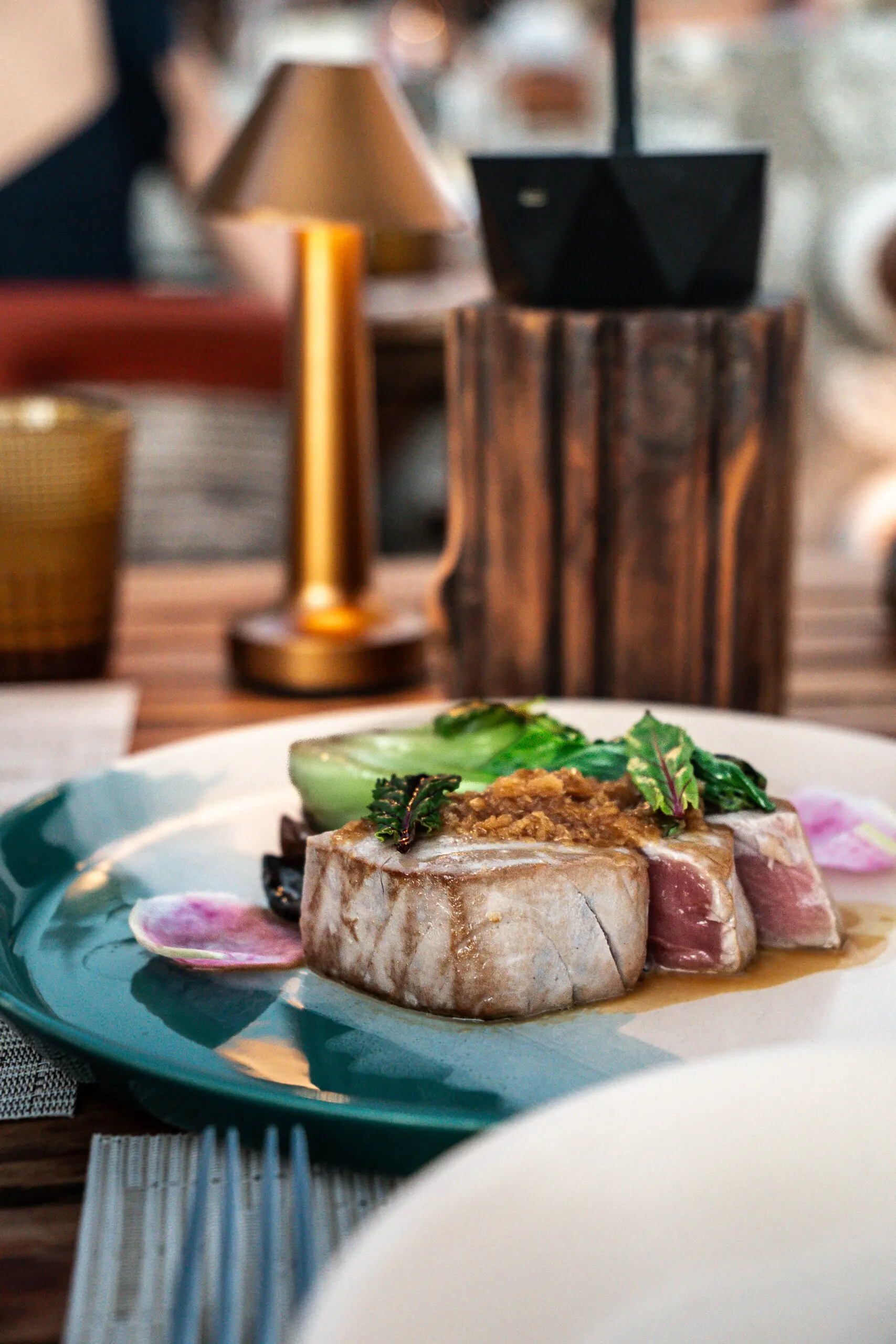 Seared tuna steak served with greens on a white plate.