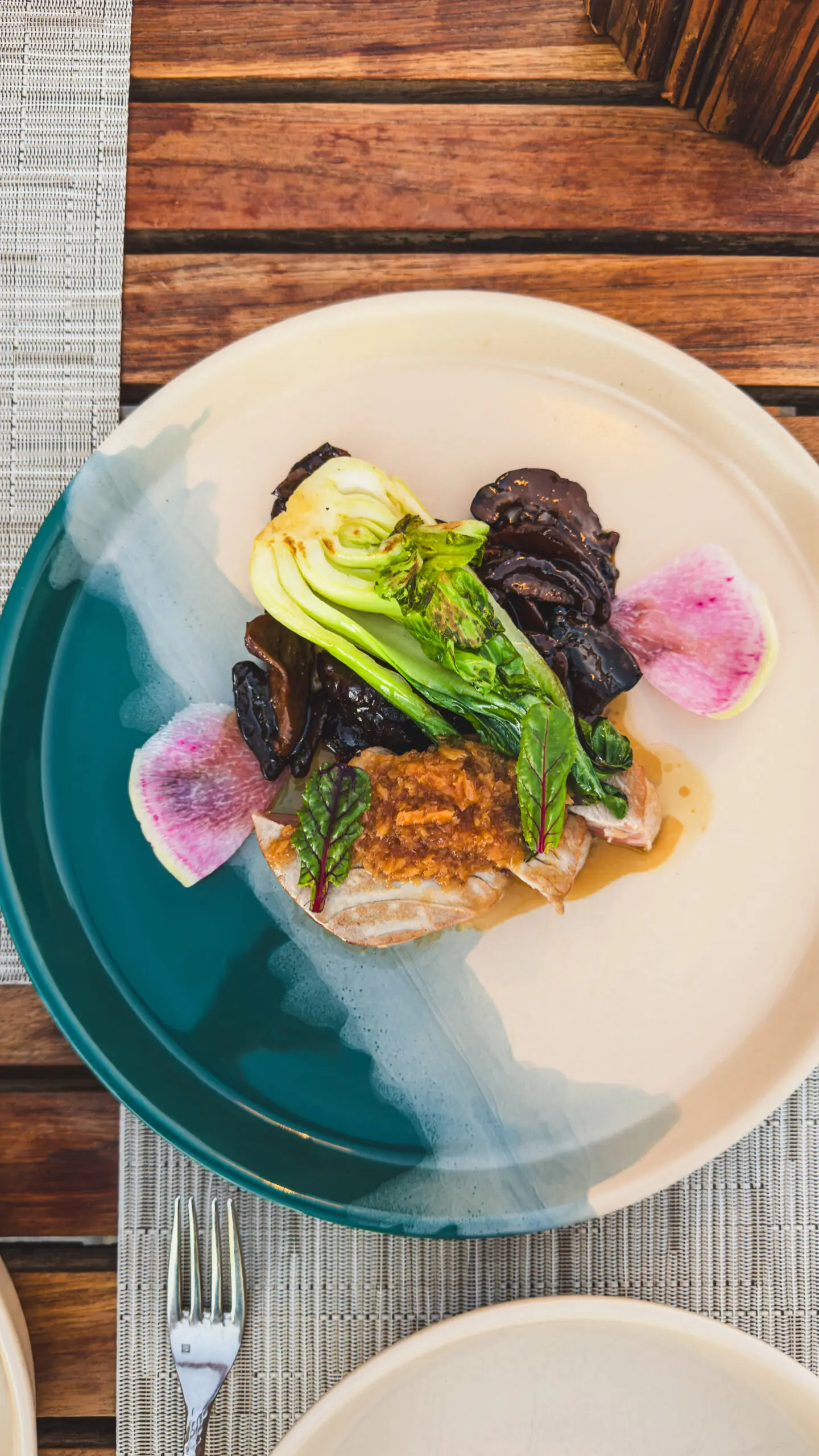Gourmet dish with grilled fish, bok choy, and colorful pickled vegetables.