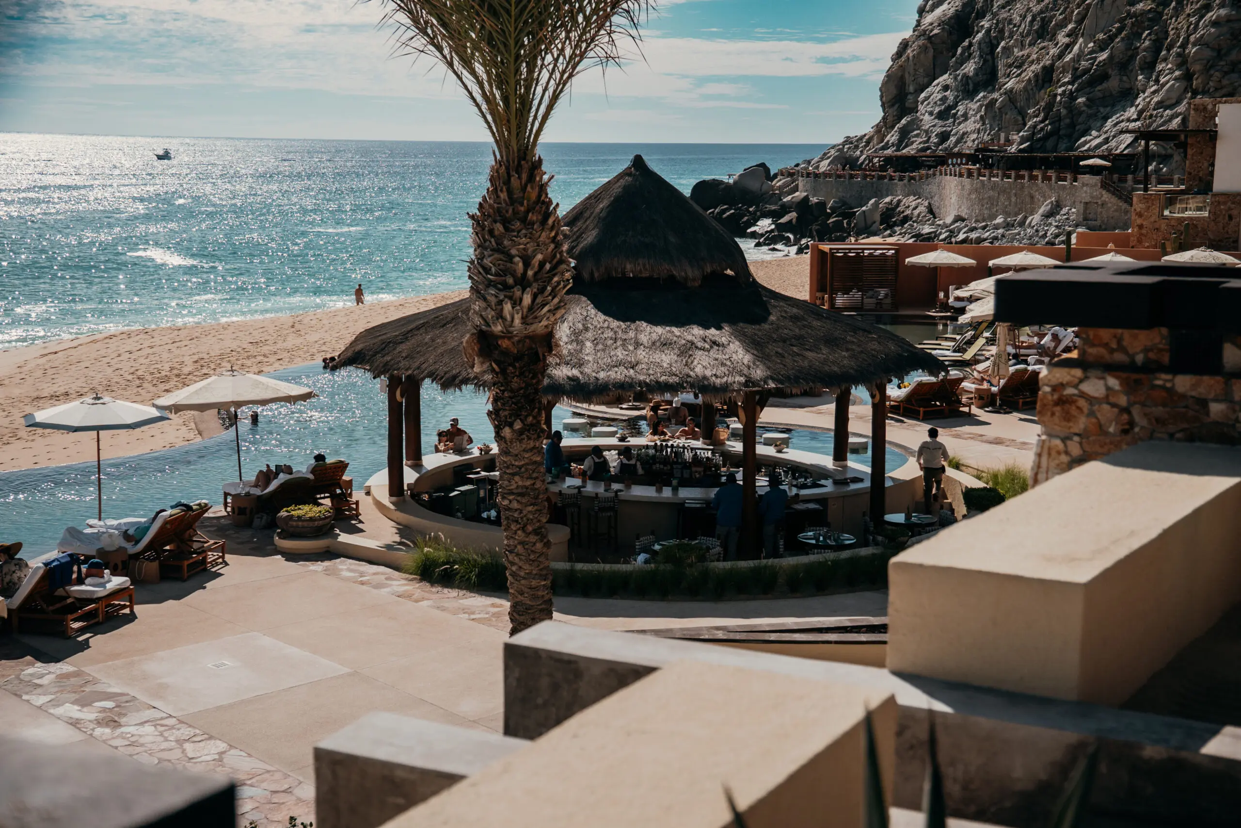 Beachfront bar with thatched roofs overlooking the ocean and rocky cliffs.