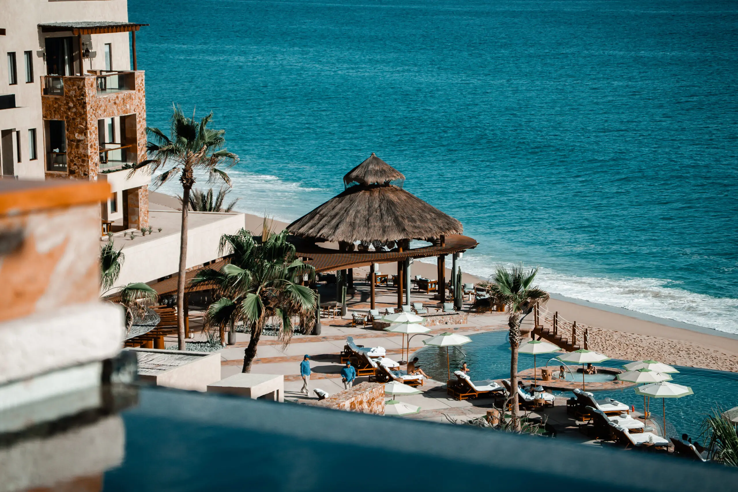 Luxury beachfront pool area with a thatched gazebo and ocean view.