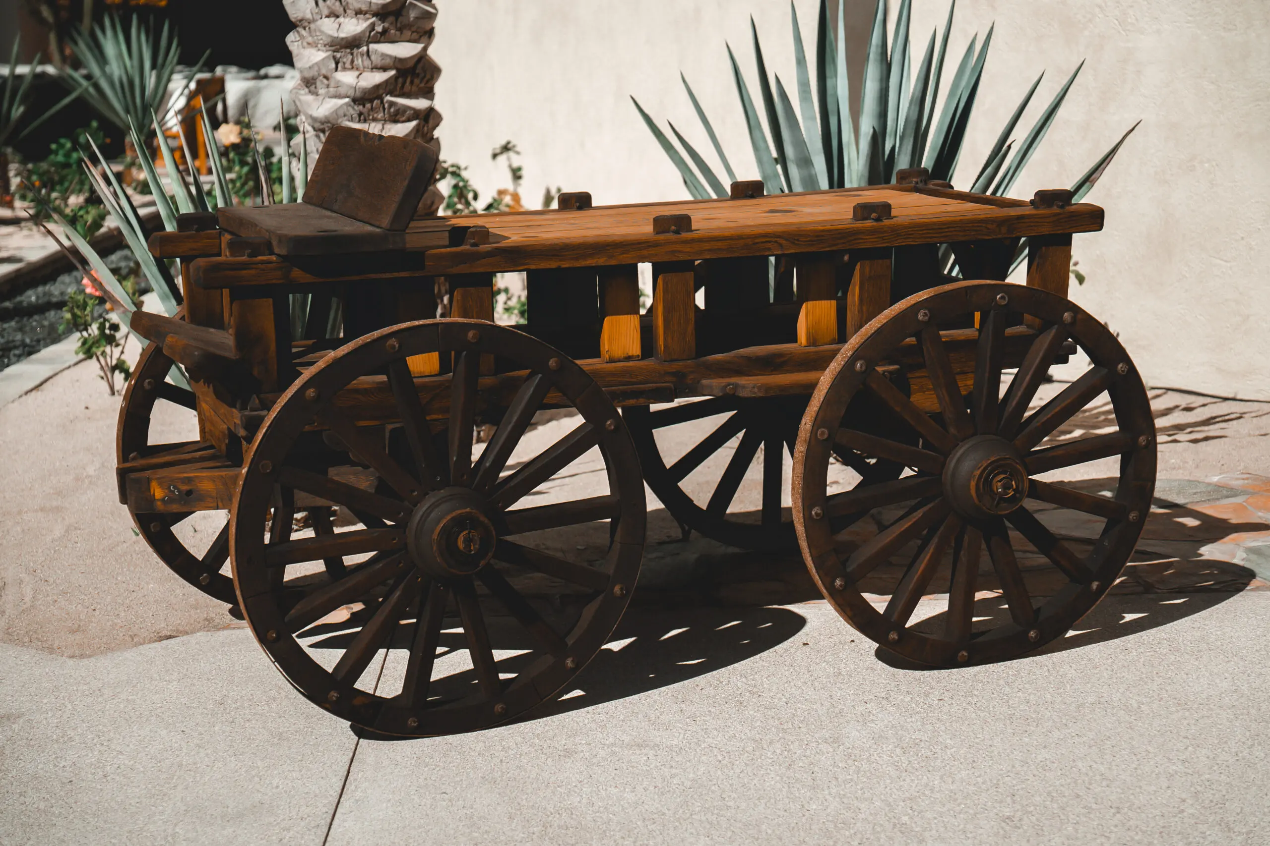 A rustic wooden wagon with large spoked wheels on a sunny patio.