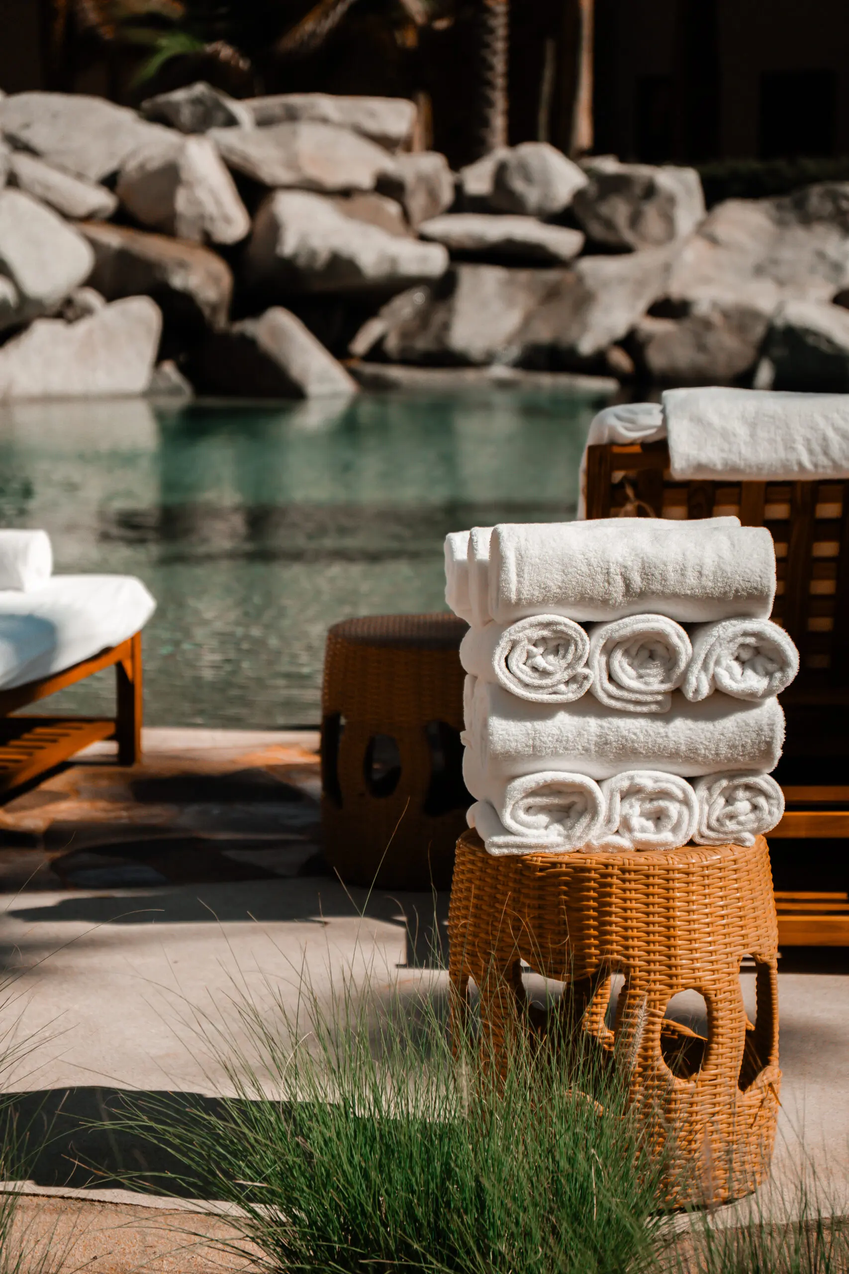 Stacked white towels by a poolside on a sunny day.