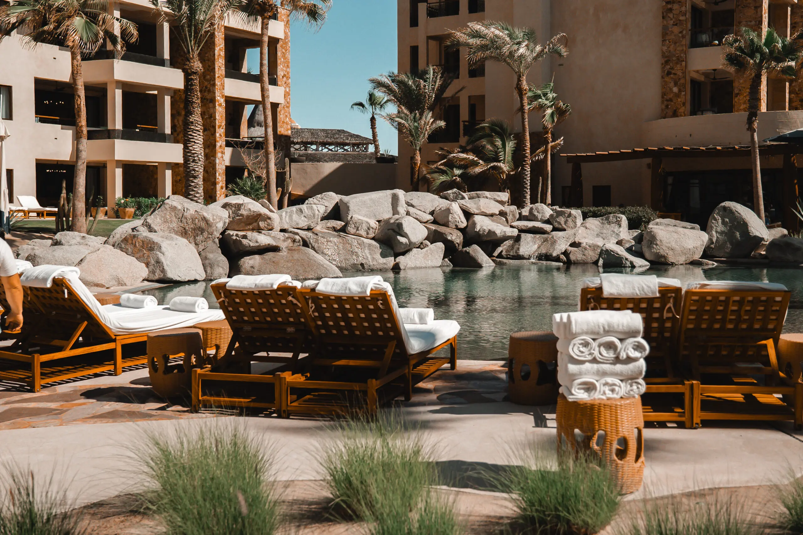 Luxurious poolside lounge chairs with cushions near a serene resort pool.