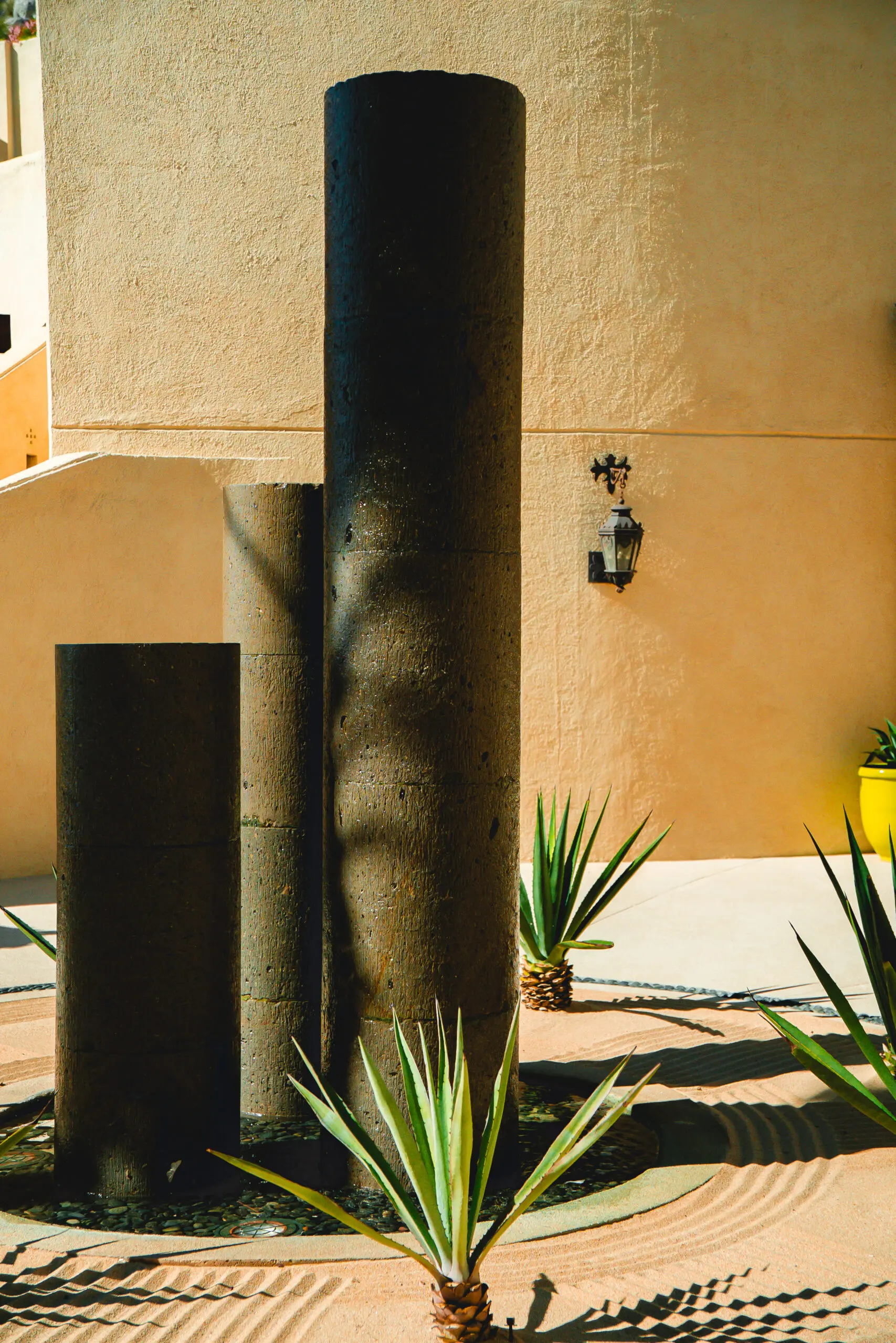 Sunlit architectural columns casting shadows near a plant and faucet.