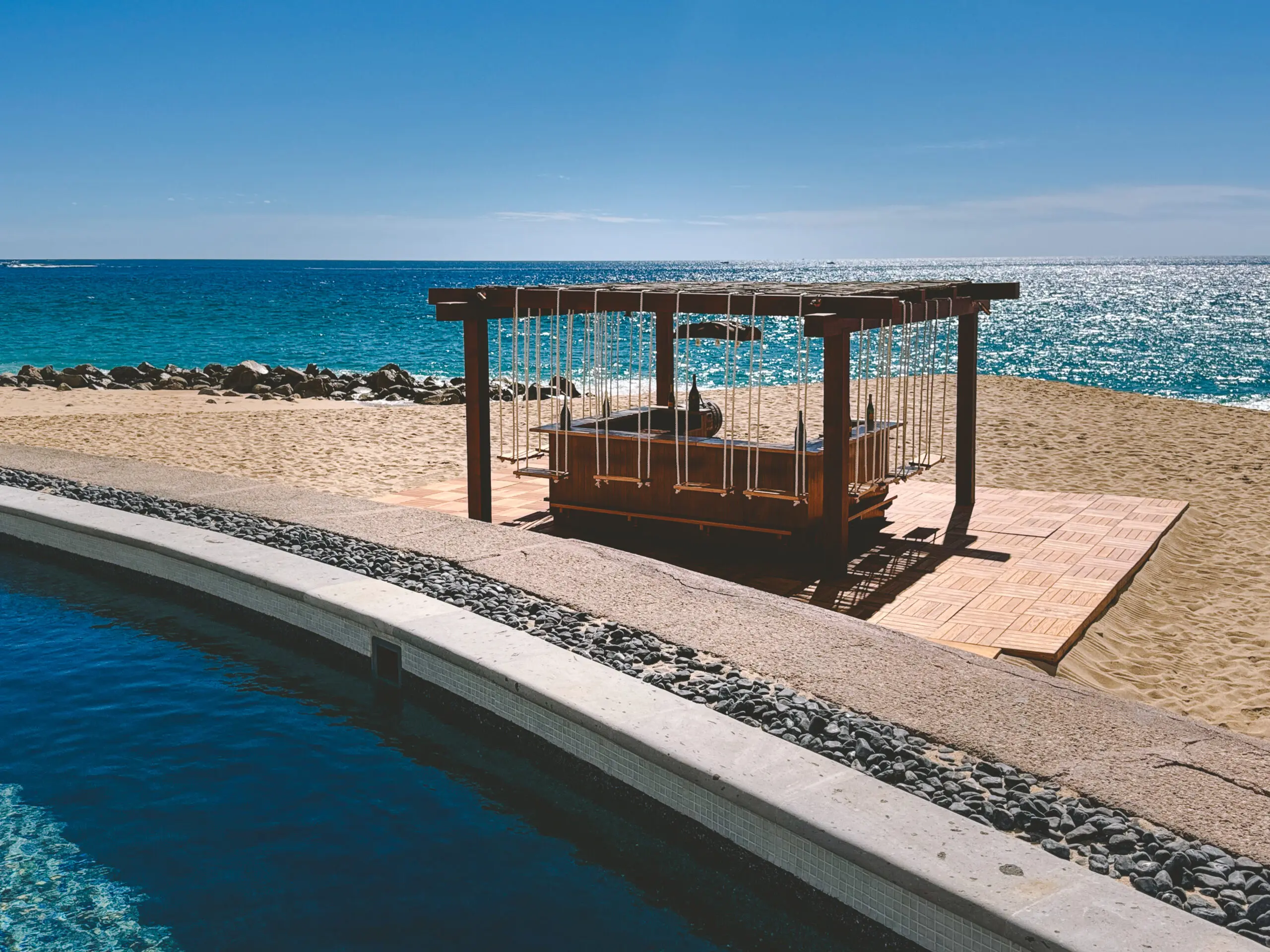 A beachside wooden gazebo with seating under clear blue skies.