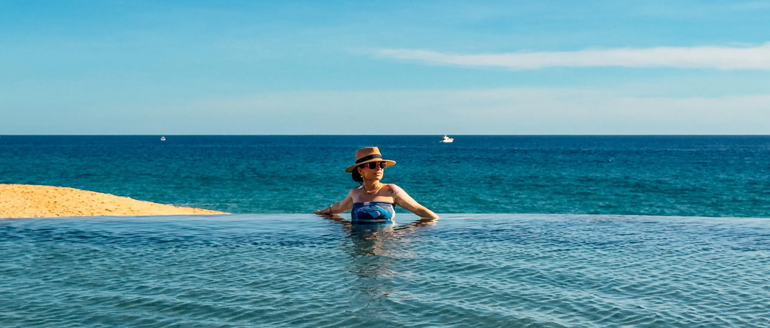 Woman in a hat relaxing in an infinity pool overlooking the ocean.