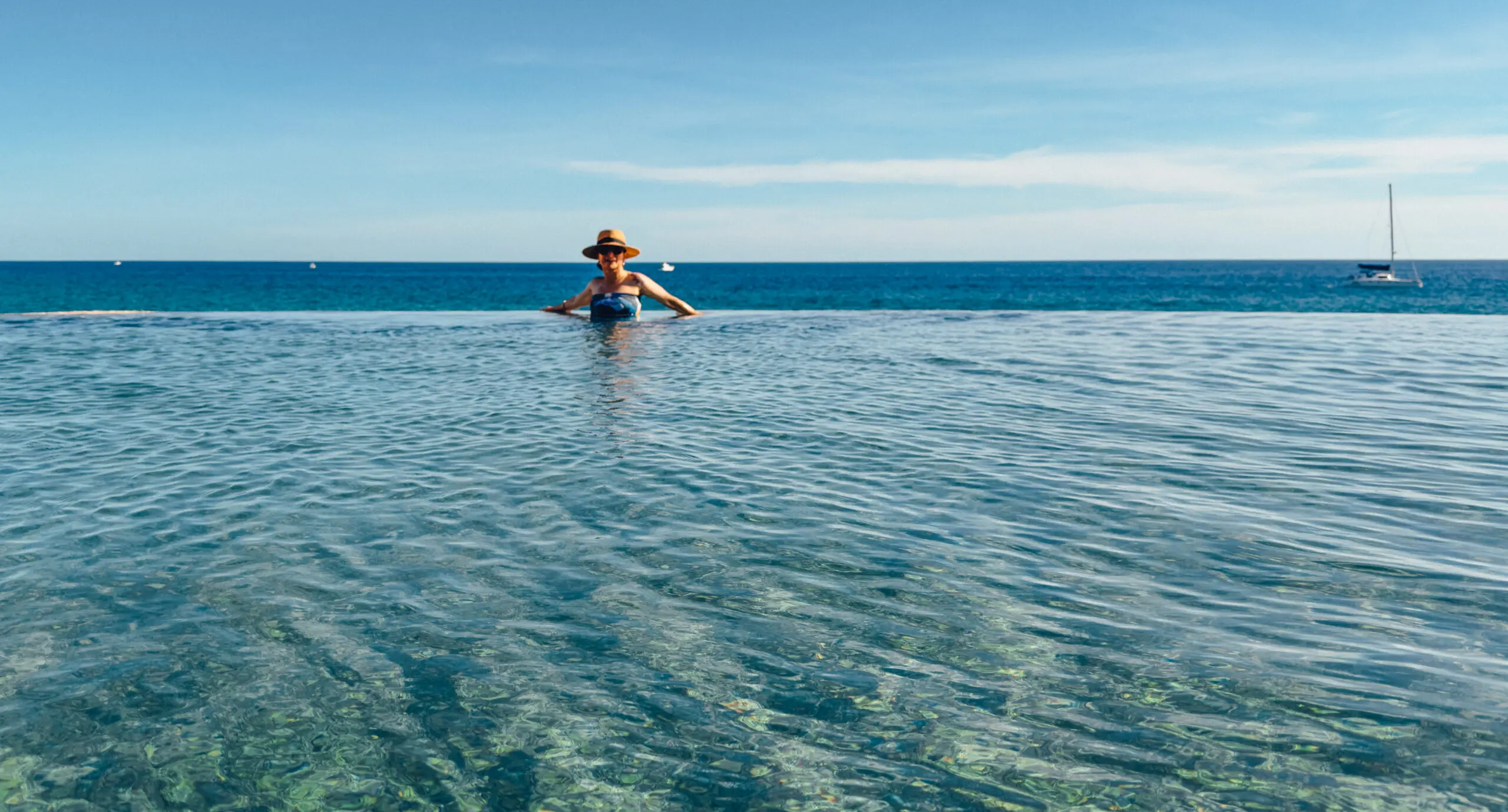 Person sitting on a paddleboard in calm, clear ocean water under a blue sky.