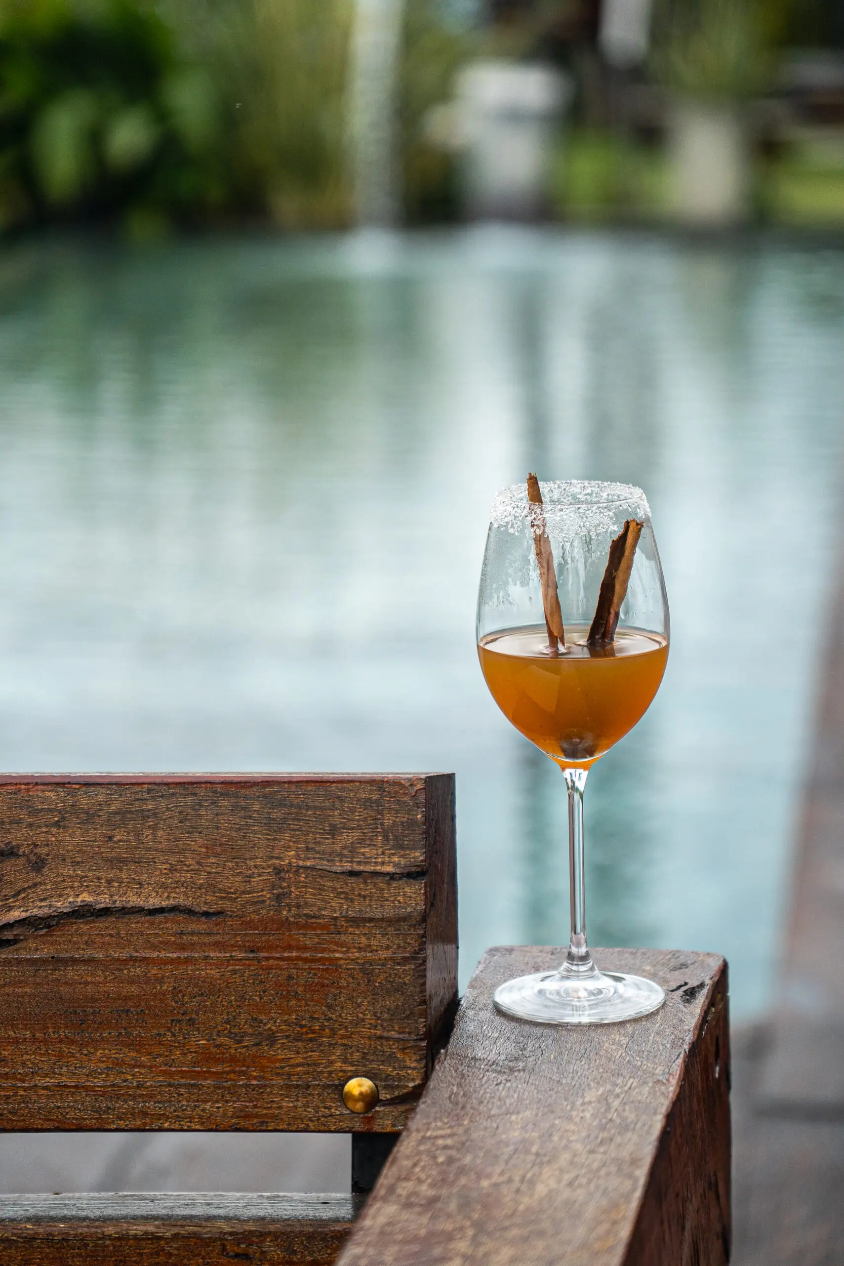 Wine glass with cinnamon sticks on a wooden table by water.