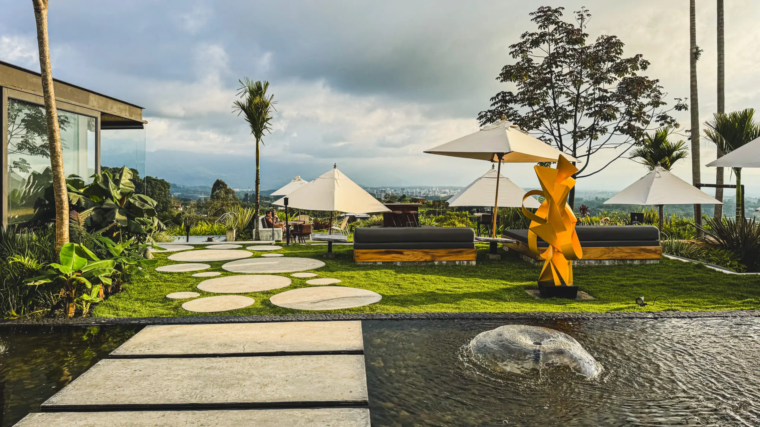 A serene outdoor seating area with umbrellas and sculptures under a cloudy sky.