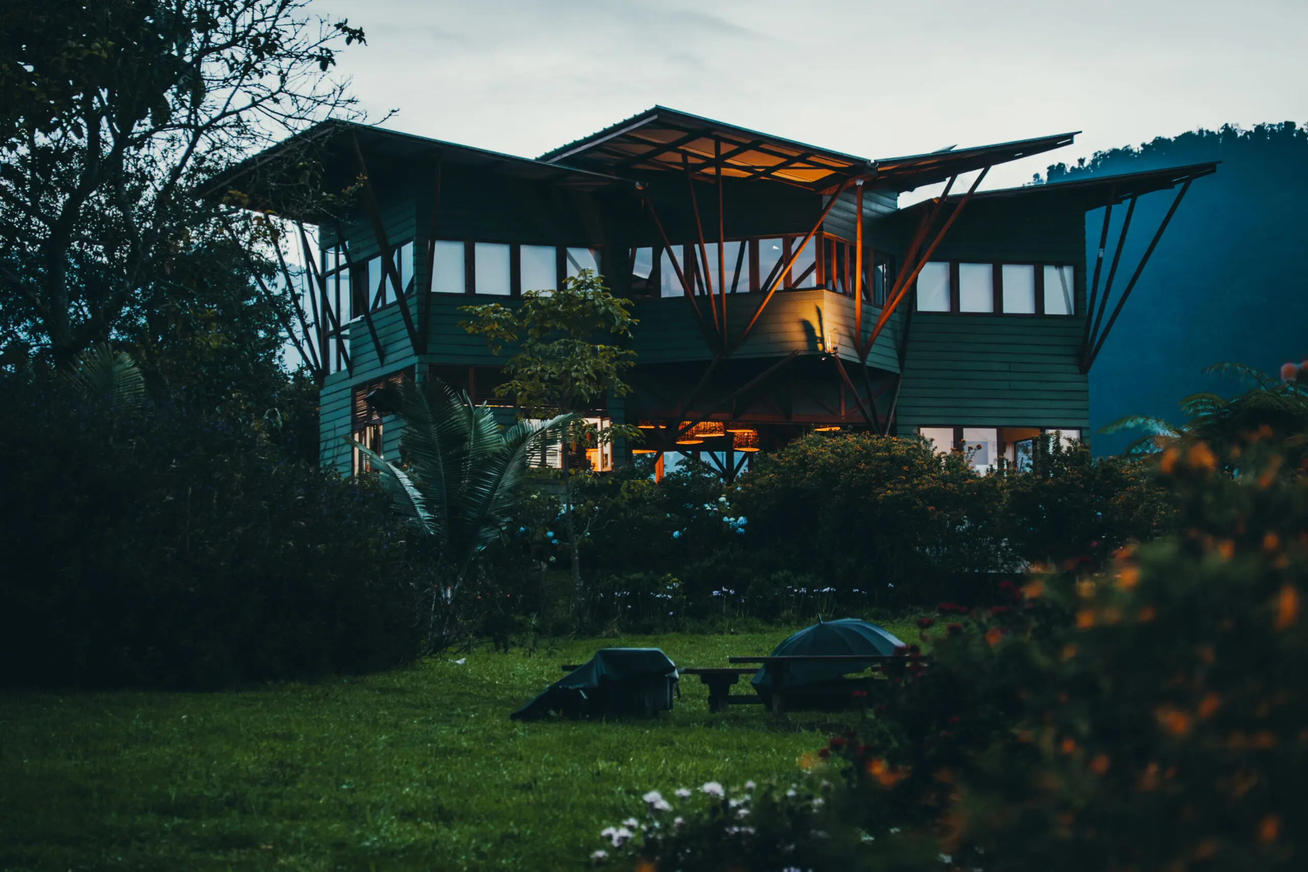 A cozy, warmly lit house at dusk surrounded by lush greenery.