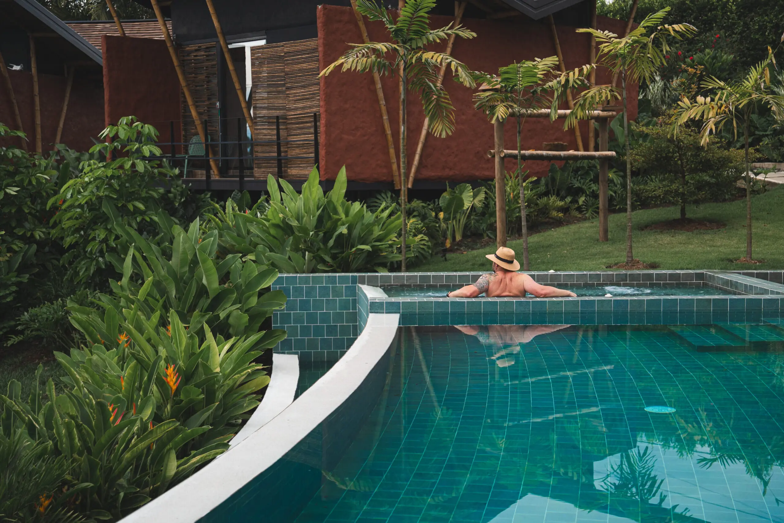 A person relaxing in a serene pool surrounded by greenery and wooden structures.