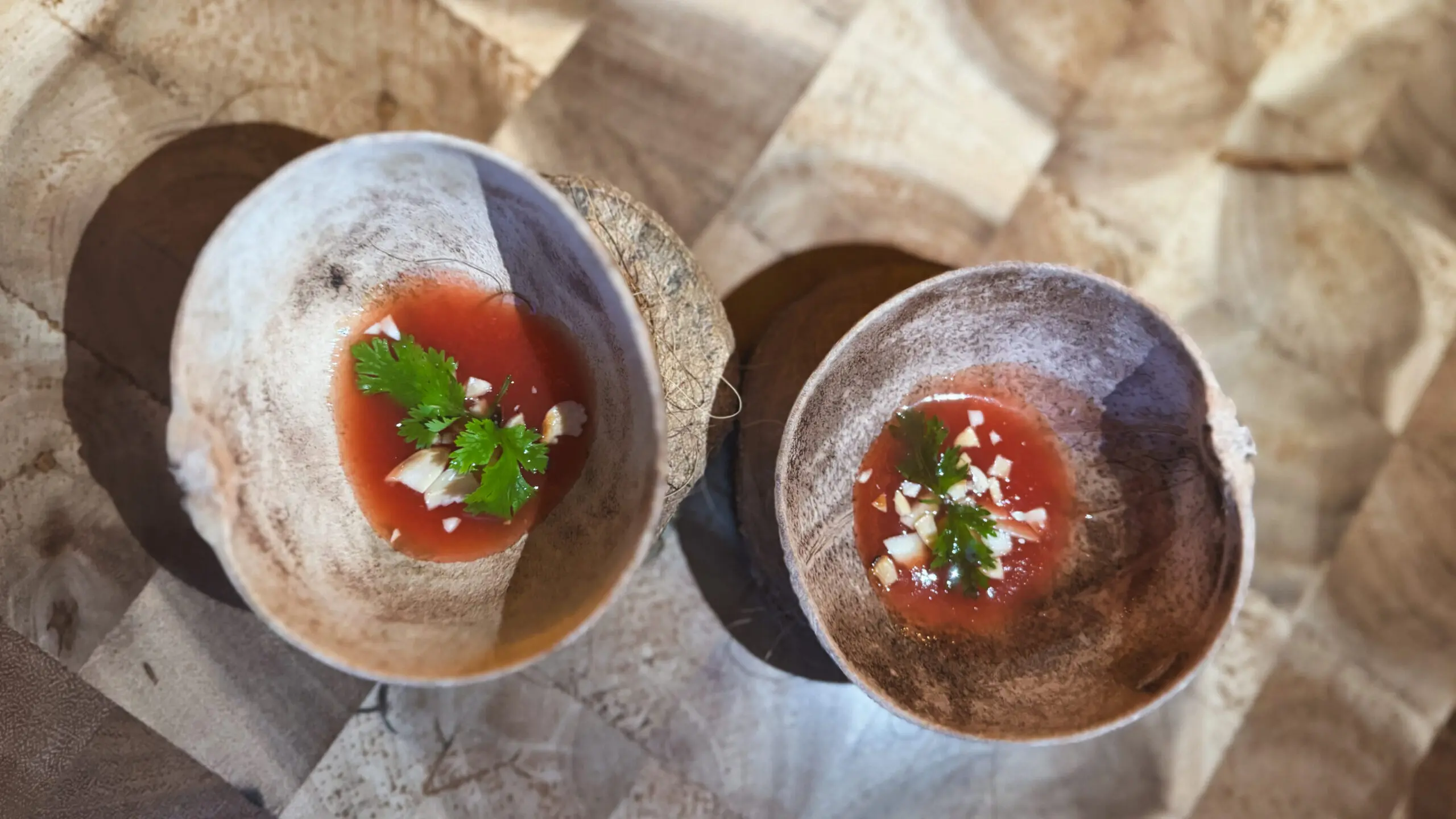 Two cups of a red sauce topped with herbs and seeds.
