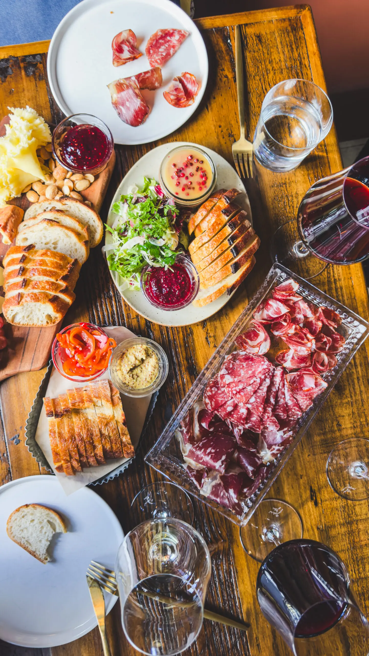 A delicious spread of grilled chicken, charcuterie, and fresh salad on a wooden table.