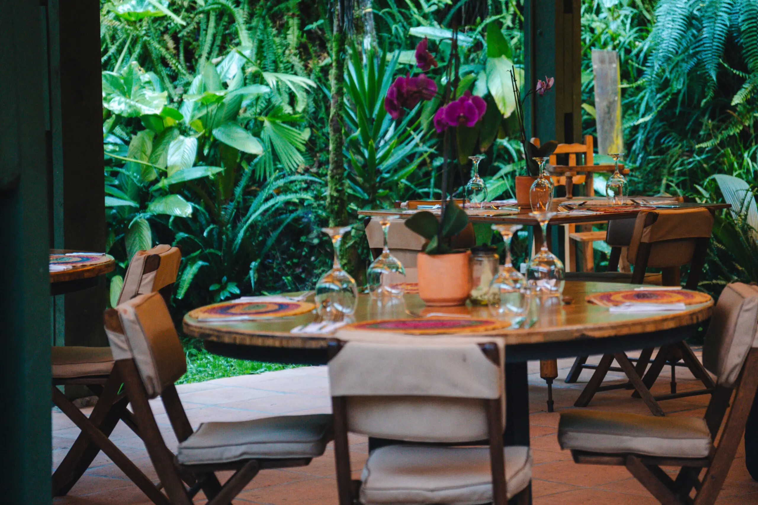 Cozy restaurant table set amid lush greenery and vibrant flowers.