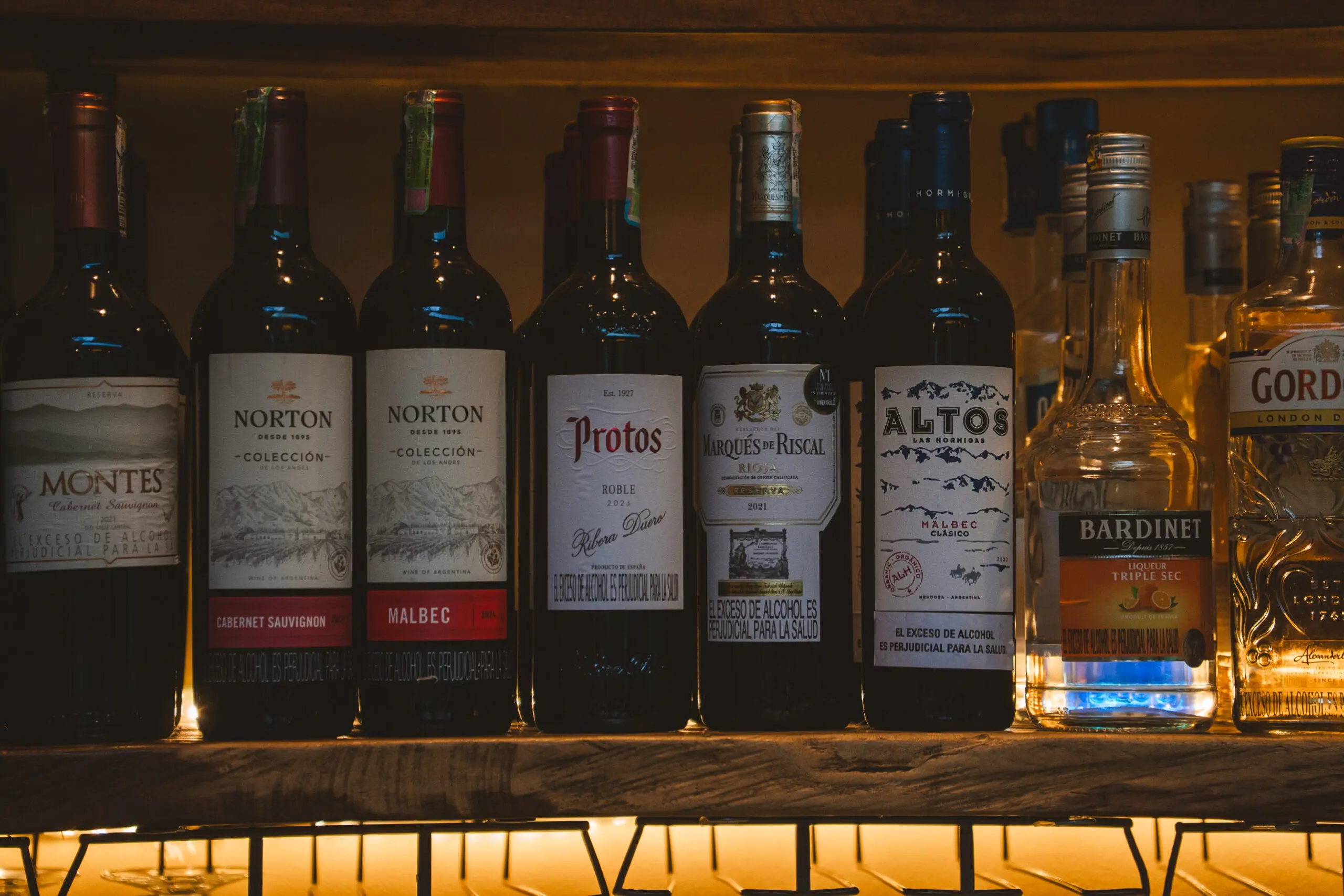 A row of various whiskey bottles on a wooden shelf with warm lighting.