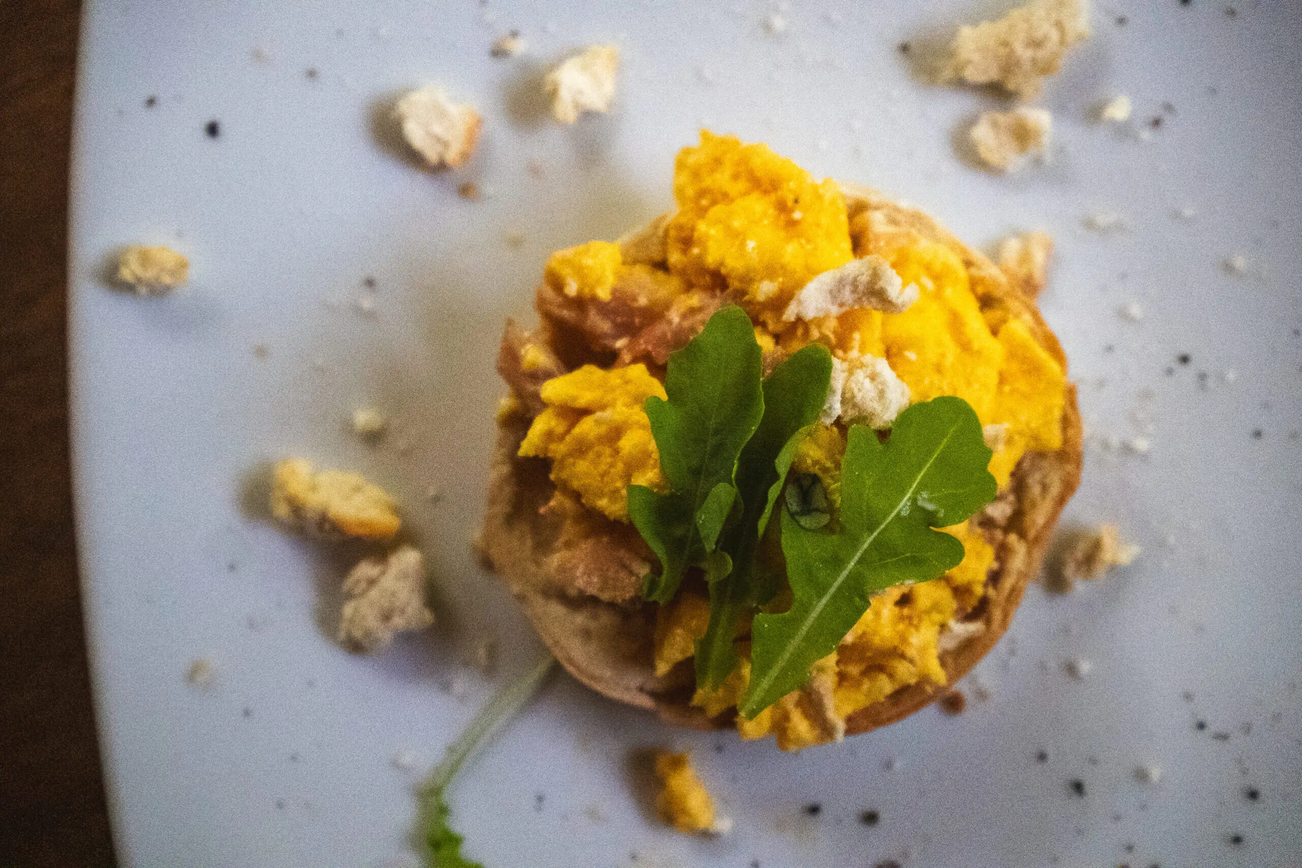 A rustic dish topped with scrambled eggs and greens on a textured surface.