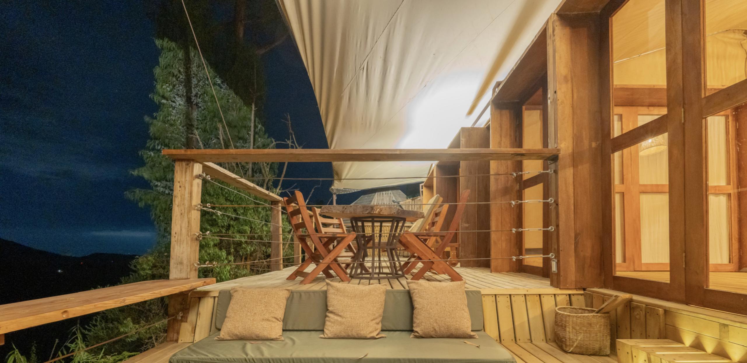 Cozy outdoor seating area with wooden chairs and table under a canopy at night.